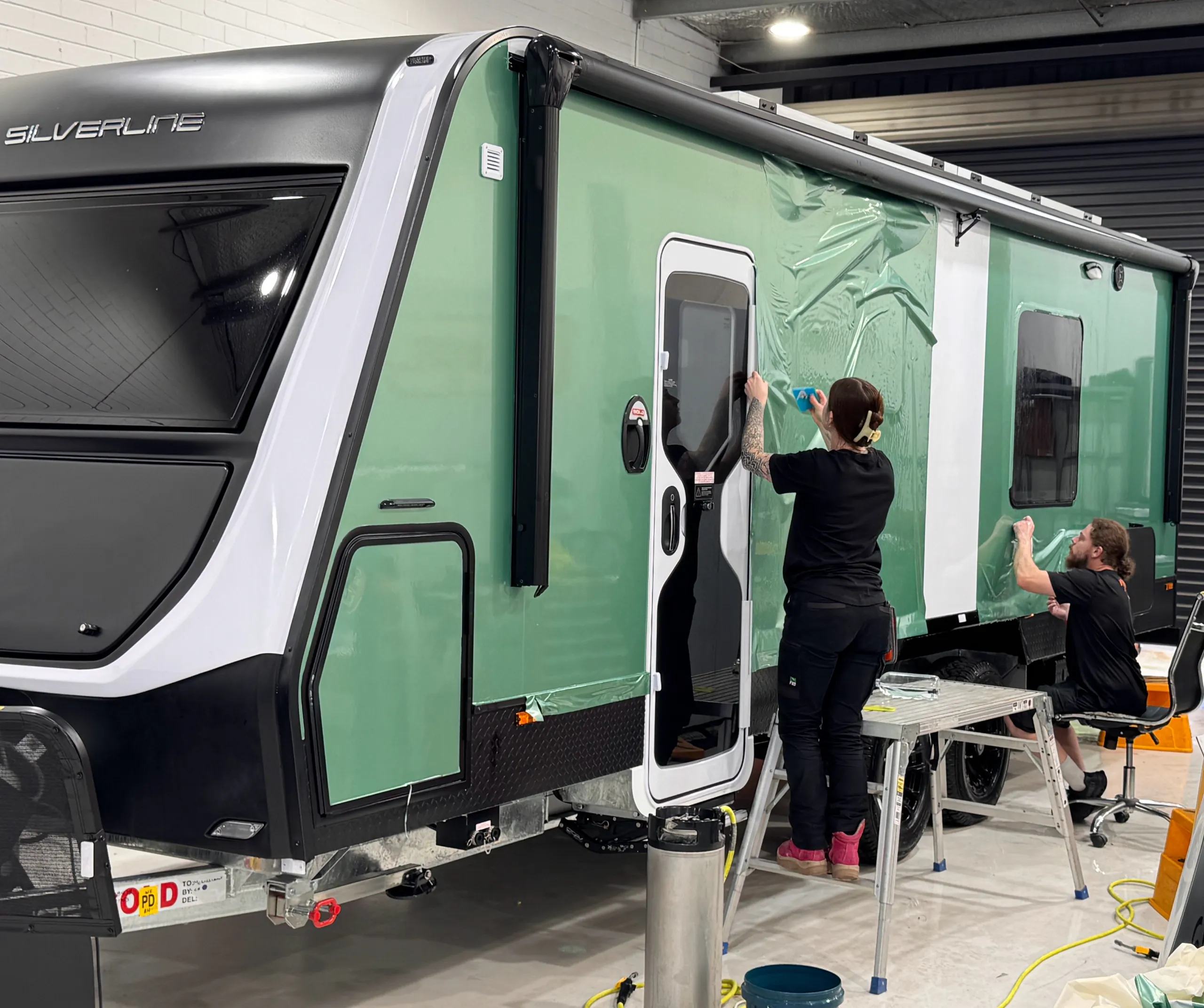 Installers working along the side of the green Jayco Silverline caravan