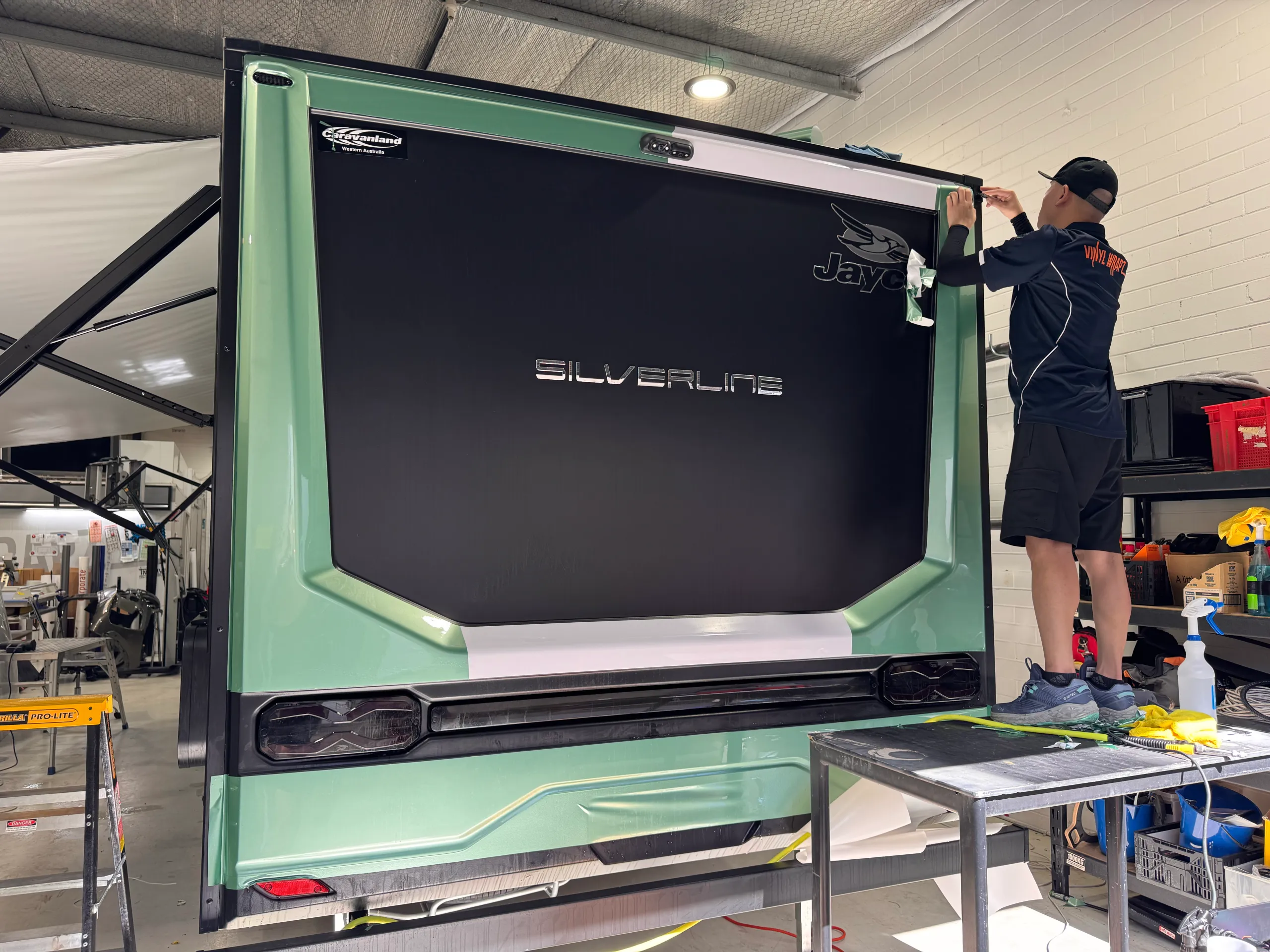 Installer working on upper trim at the rear of the green Jayco caravan