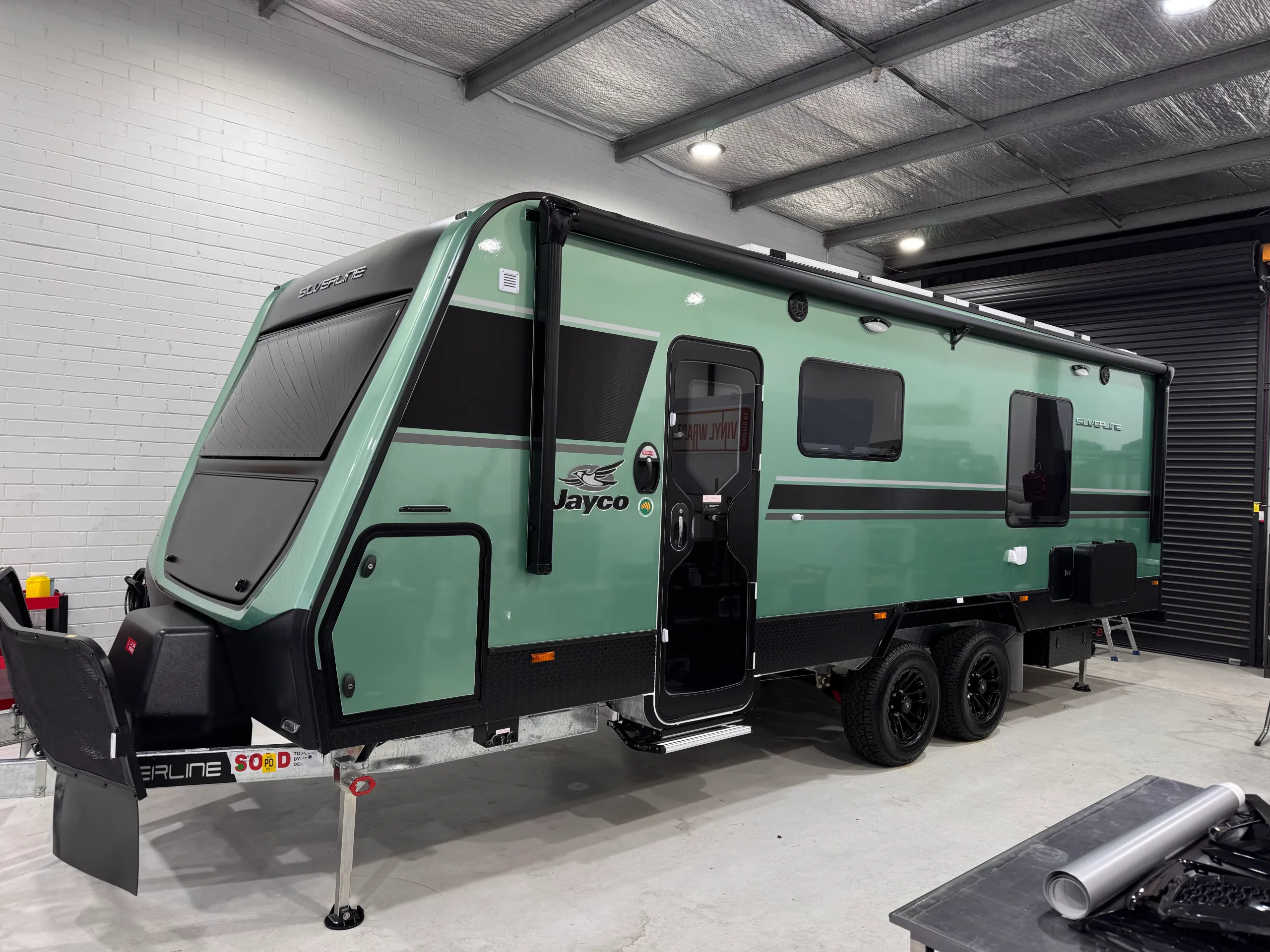 Green Jayco Silverline caravan with black graphics viewed from the front quarter inside the workshop
