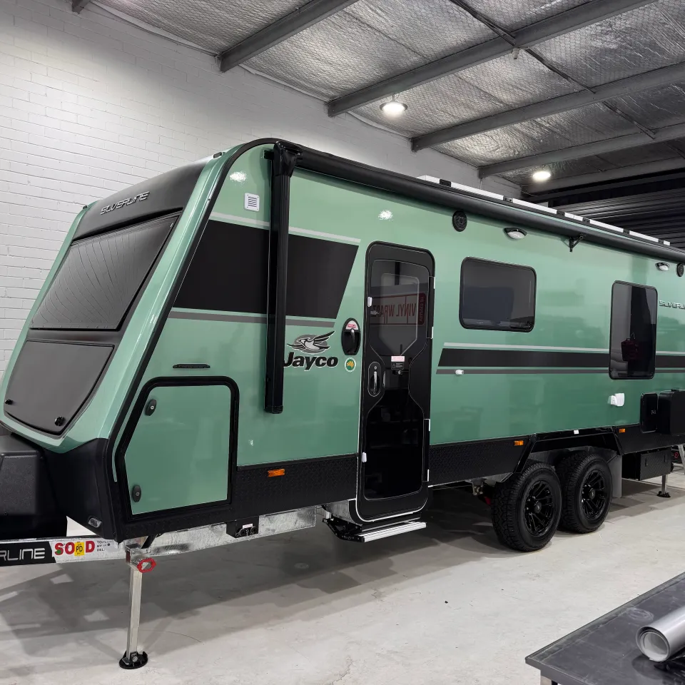 Green Jayco Silverline caravan with black graphics viewed from the front quarter inside the workshop