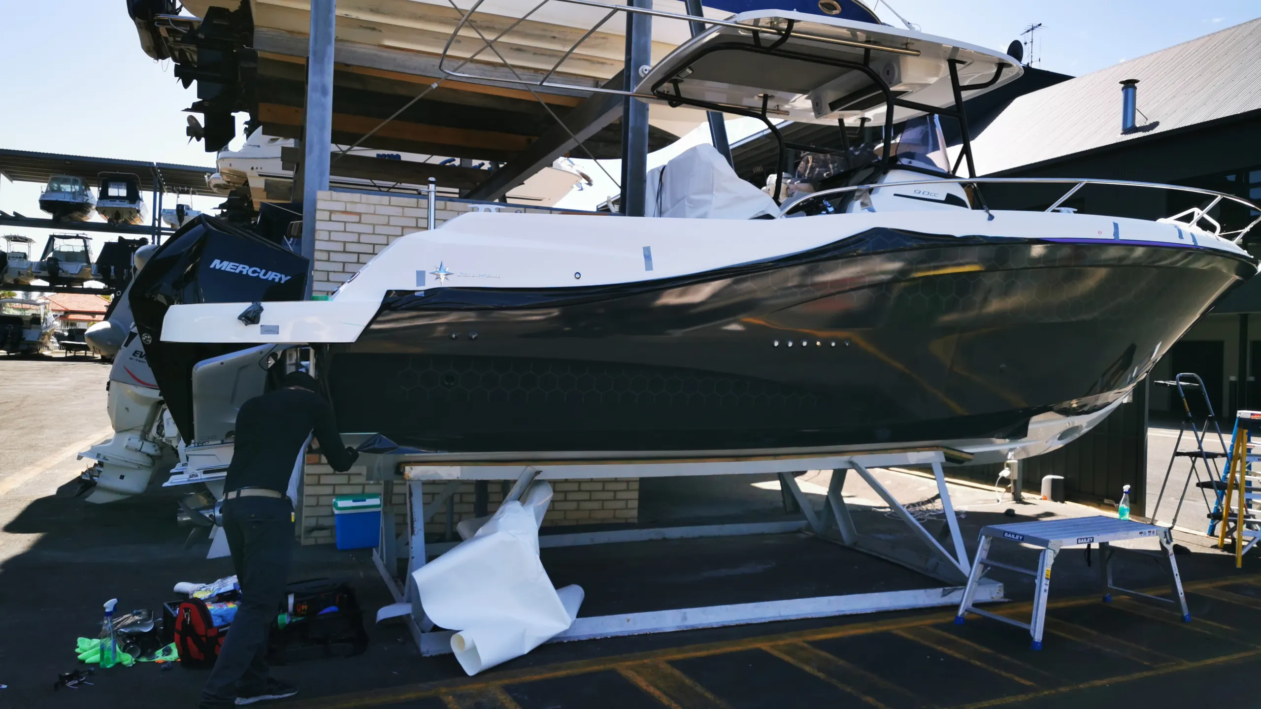 Back-facing installer trimming dark printed film near the boat stern
