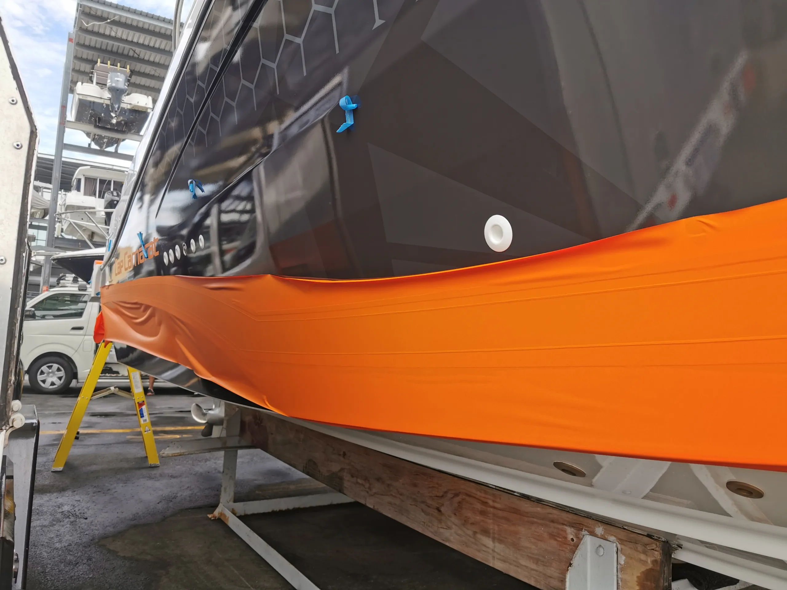 Orange film stretched beneath the dark honeycomb hull graphics during installation