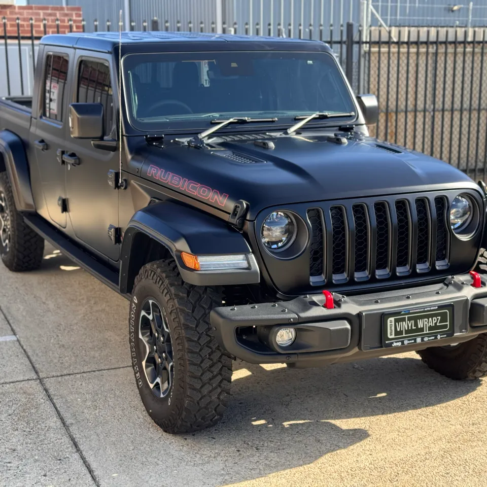 Matte black Jeep Gladiator Rubicon parked outside by a fence