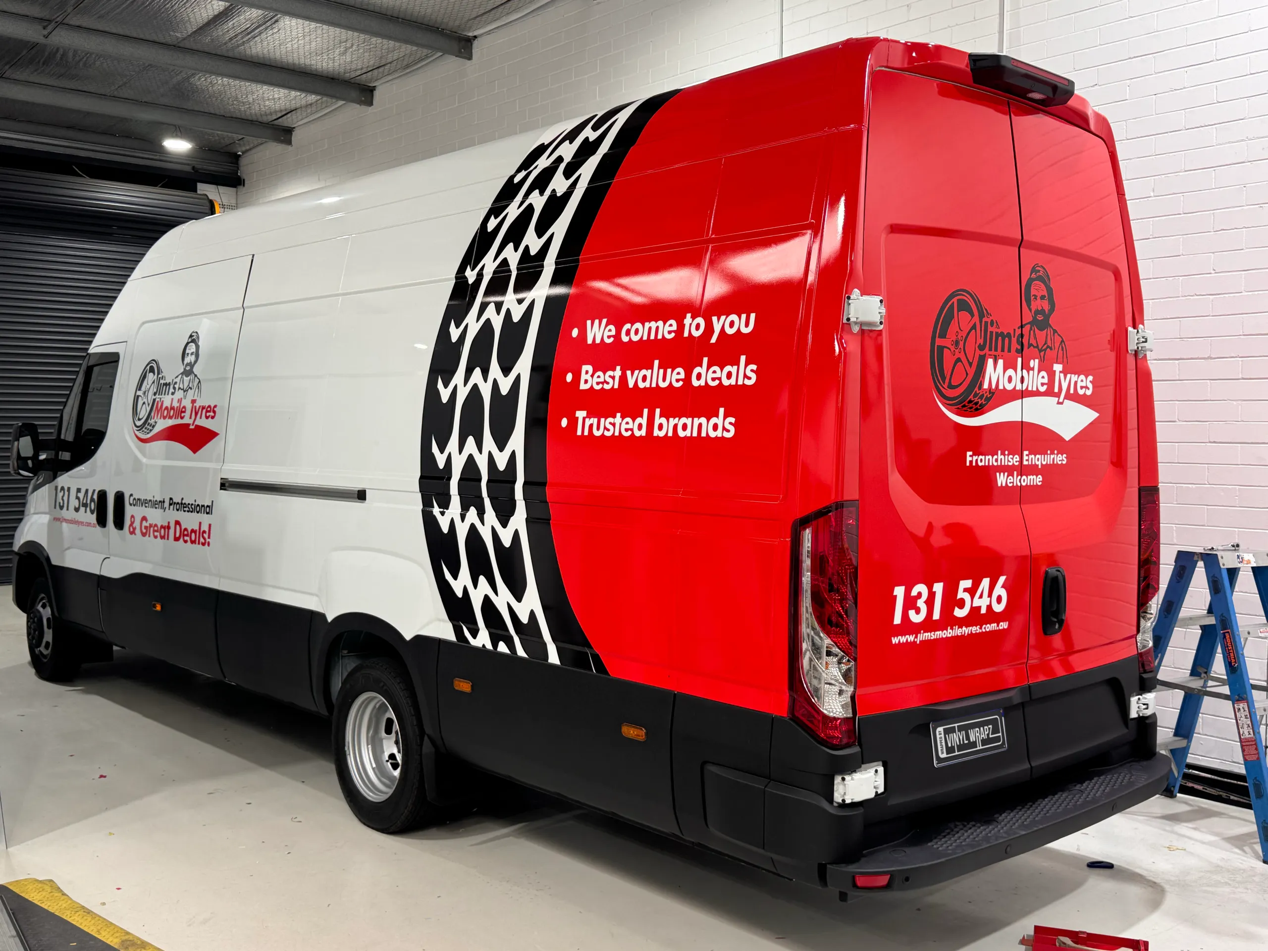 Jim's Mobile Tyres Iveco Daily rear quarter with red panels and tyre-tread graphics inside the workshop