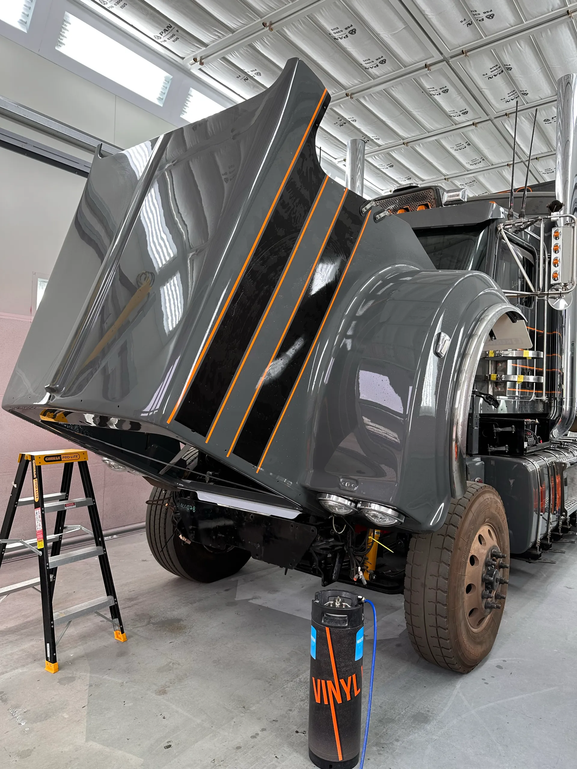 Grey Kenworth truck with its striped bonnet tilted forward in the workshop