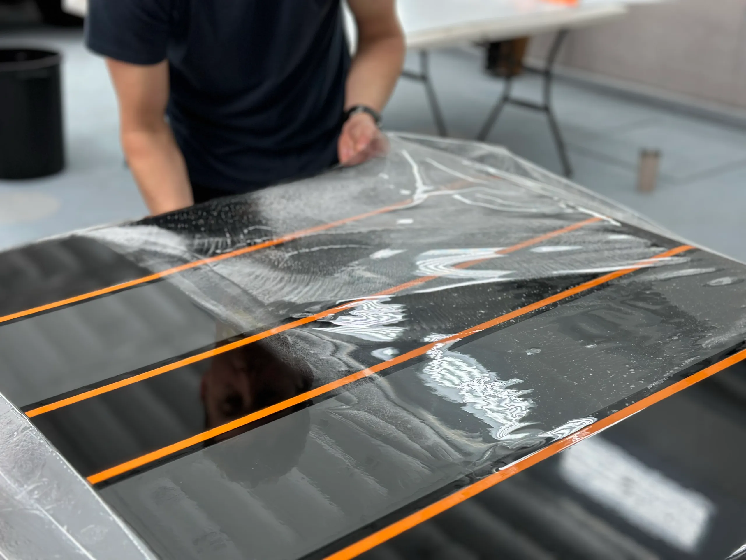 Clear film laid over a grey truck panel with black stripes and orange pinstriping