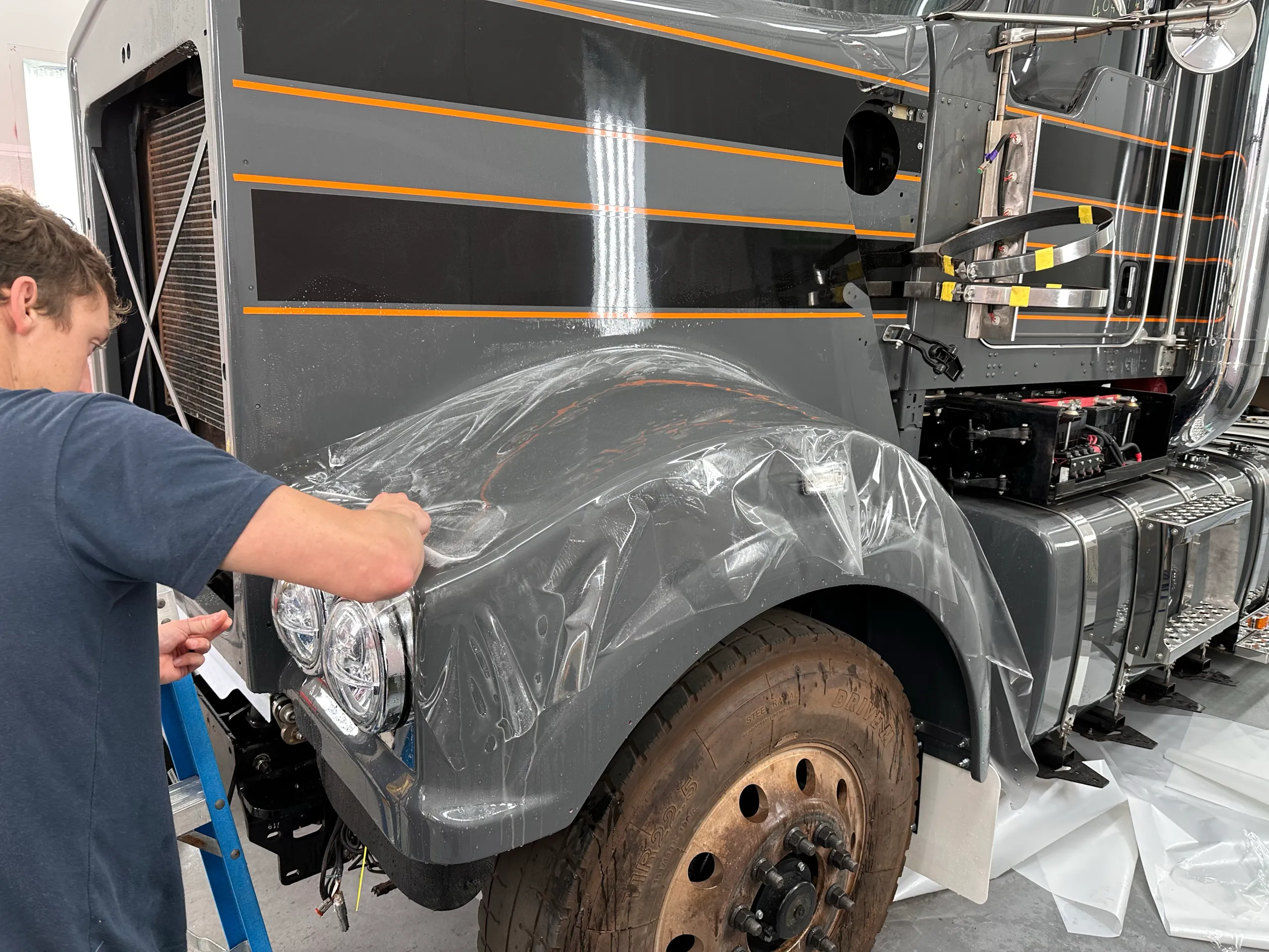 Installer fitting clear film around the grey truck front guard and headlight