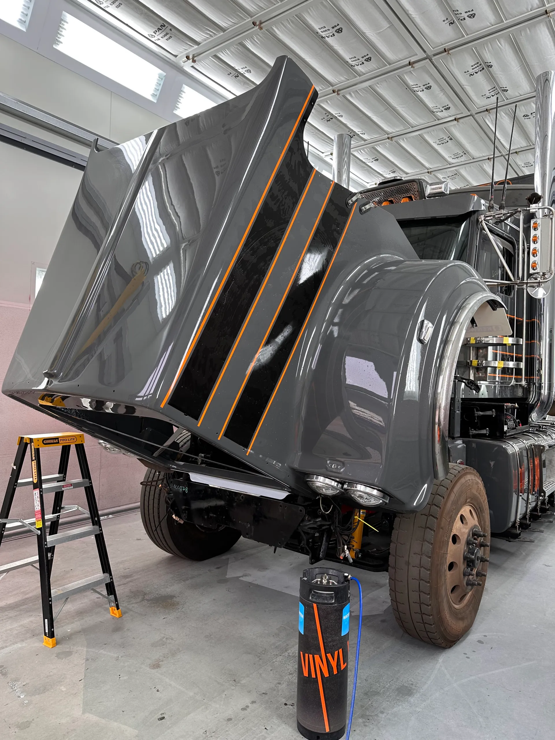 Grey truck bonnet tilted forward, showing black stripes with orange edges