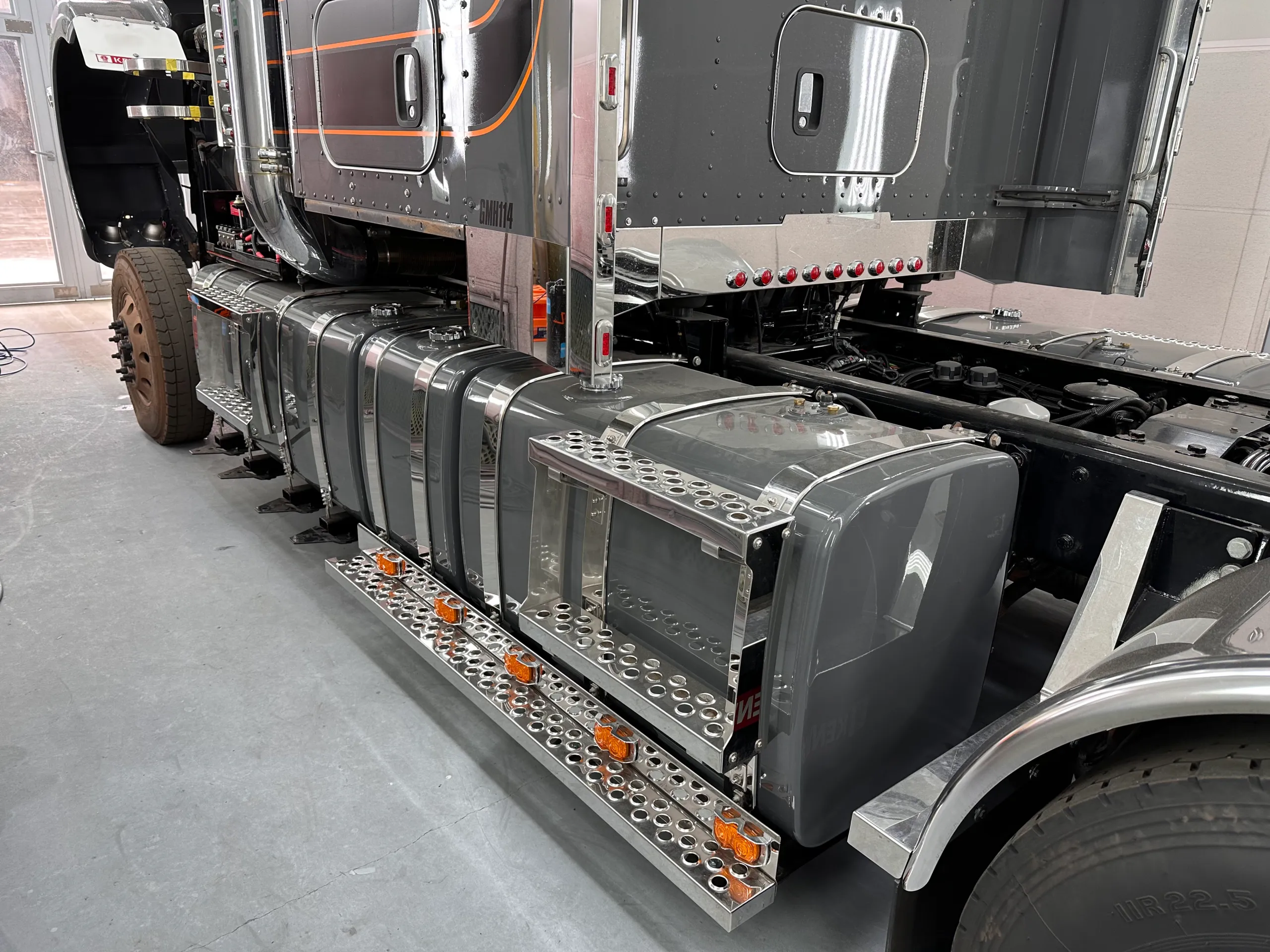 Chrome fuel tanks and side steps beside the grey Kenworth cab
