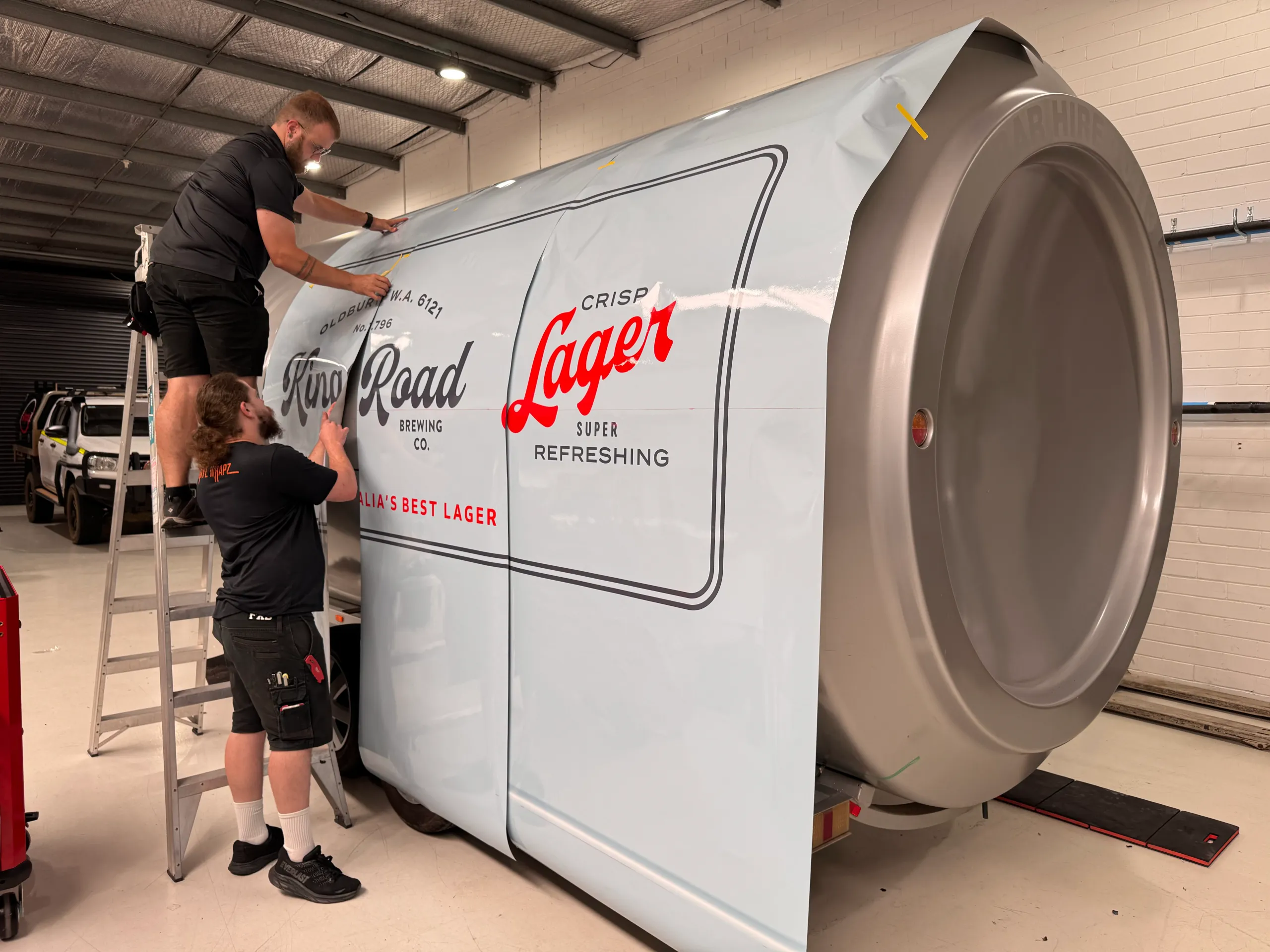 Two installers smoothing printed graphics around the King Road can trailer