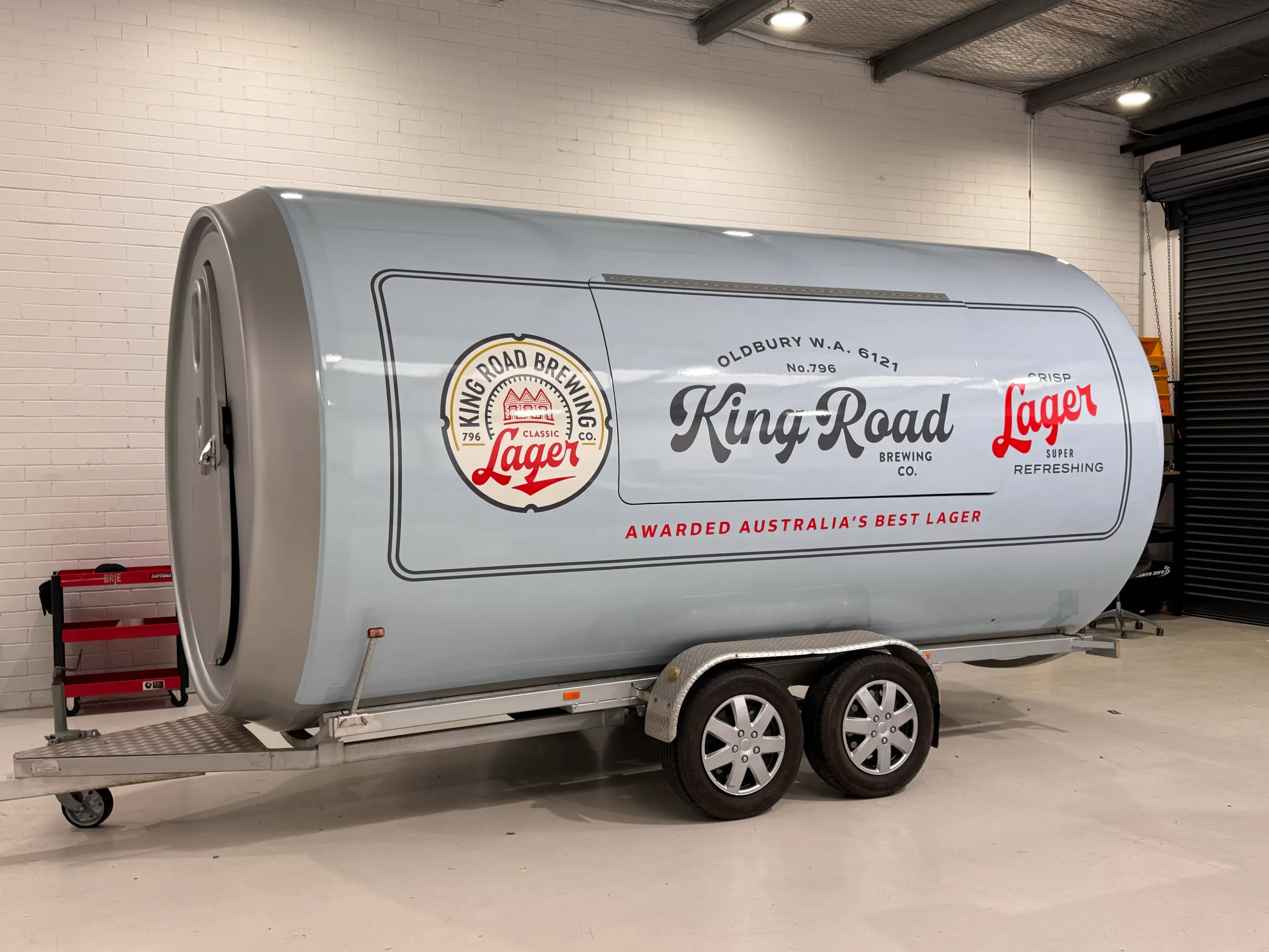 Pale blue King Road Lager can-shaped trailer with its serving hatch closed inside the workshop