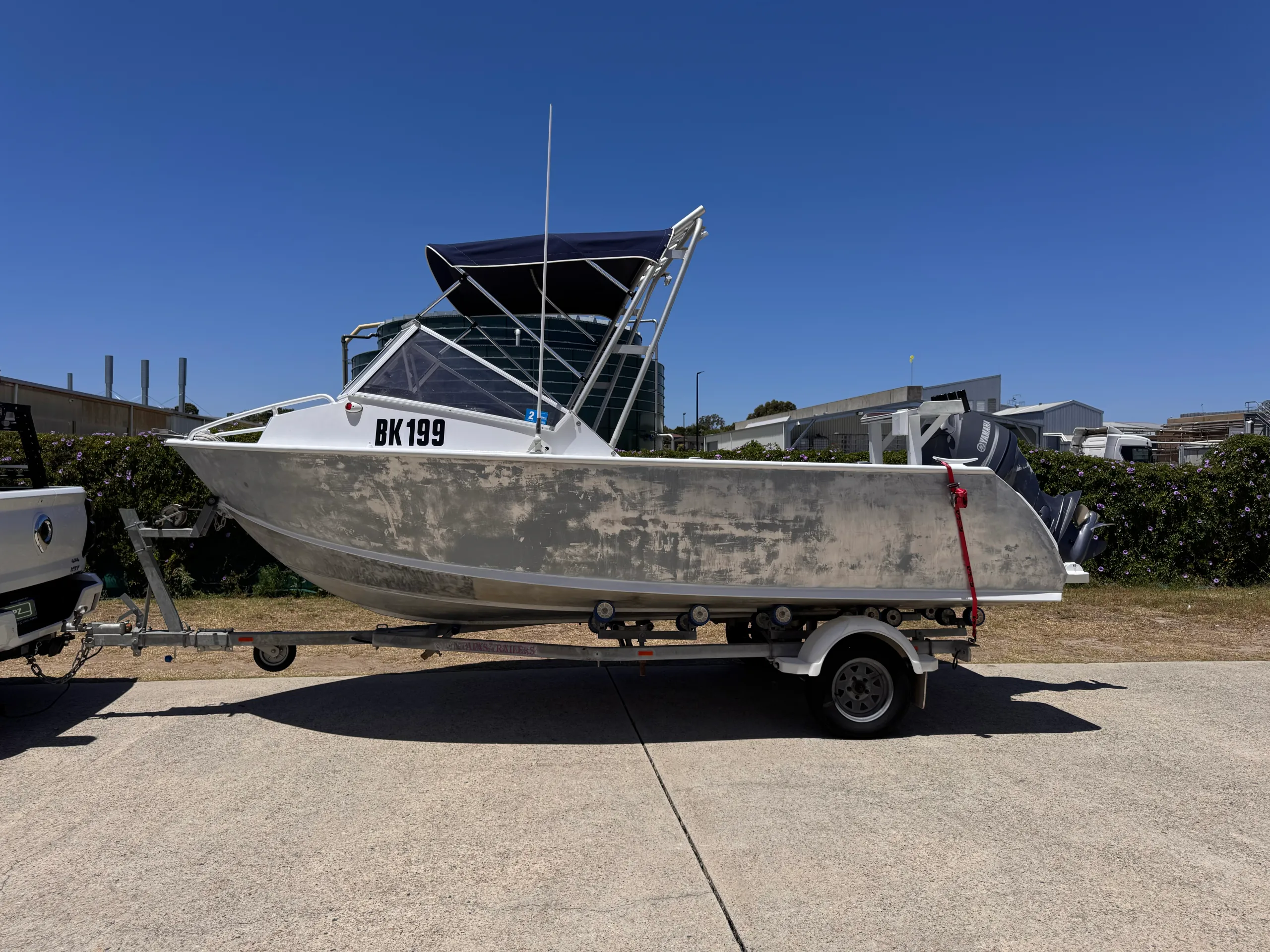 Bare aluminium boat on its trailer outdoors, with its bimini raised