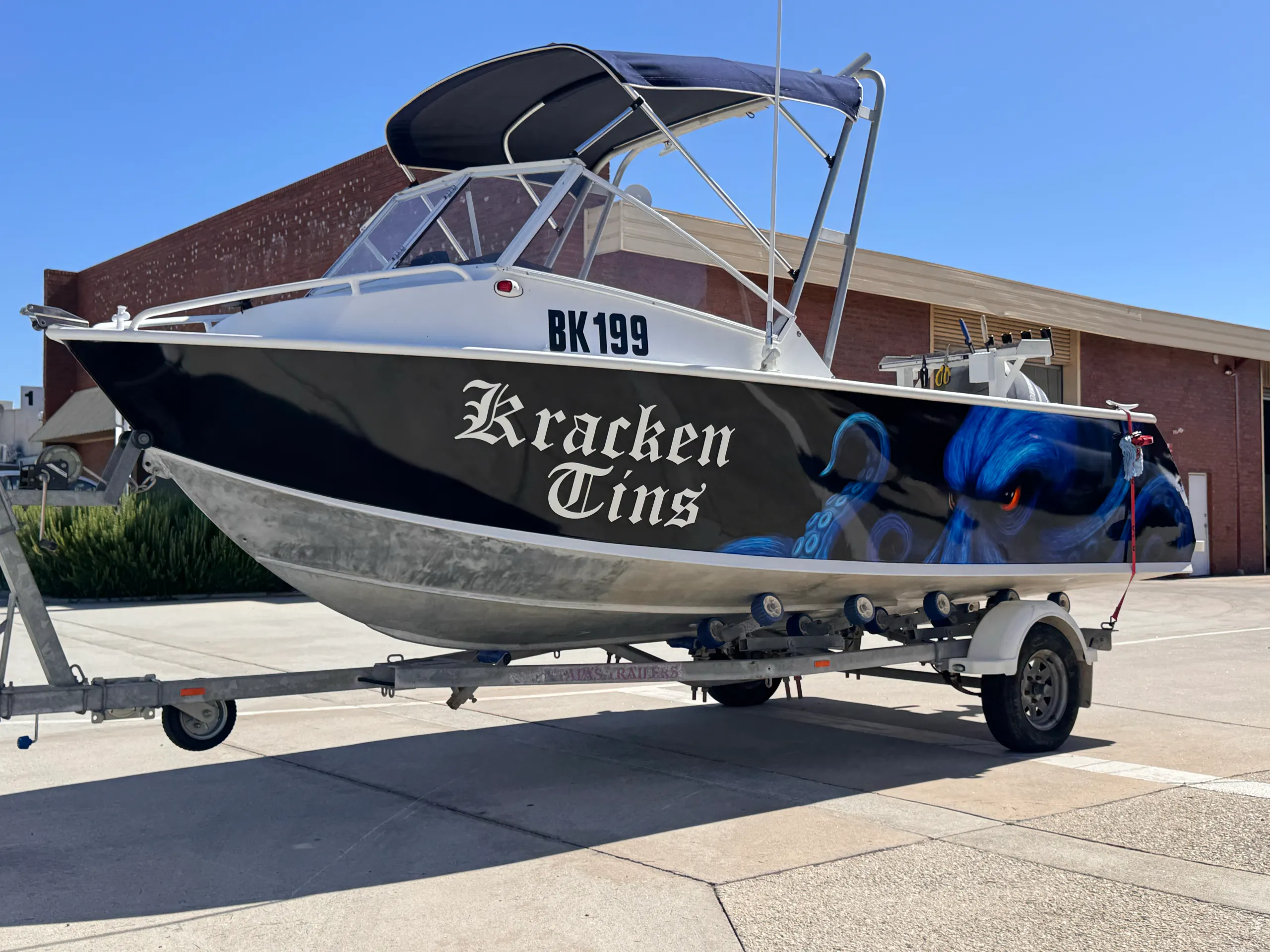 Bow-quarter view of the Kracken Tins boat with blue octopus artwork on a black hull