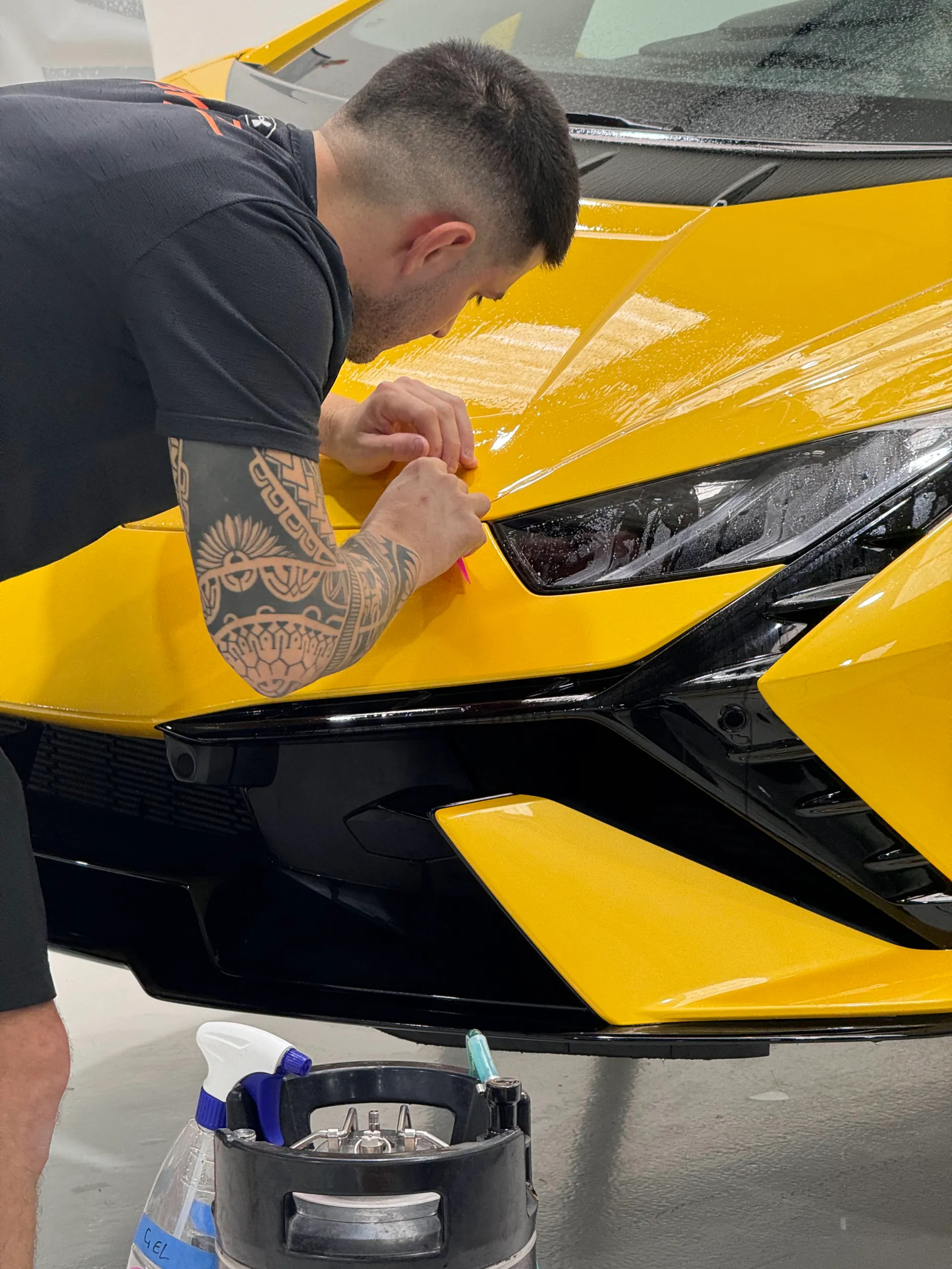 Installer fitting clear film around the yellow Lamborghini Huracan Tecnica bonnet and headlight