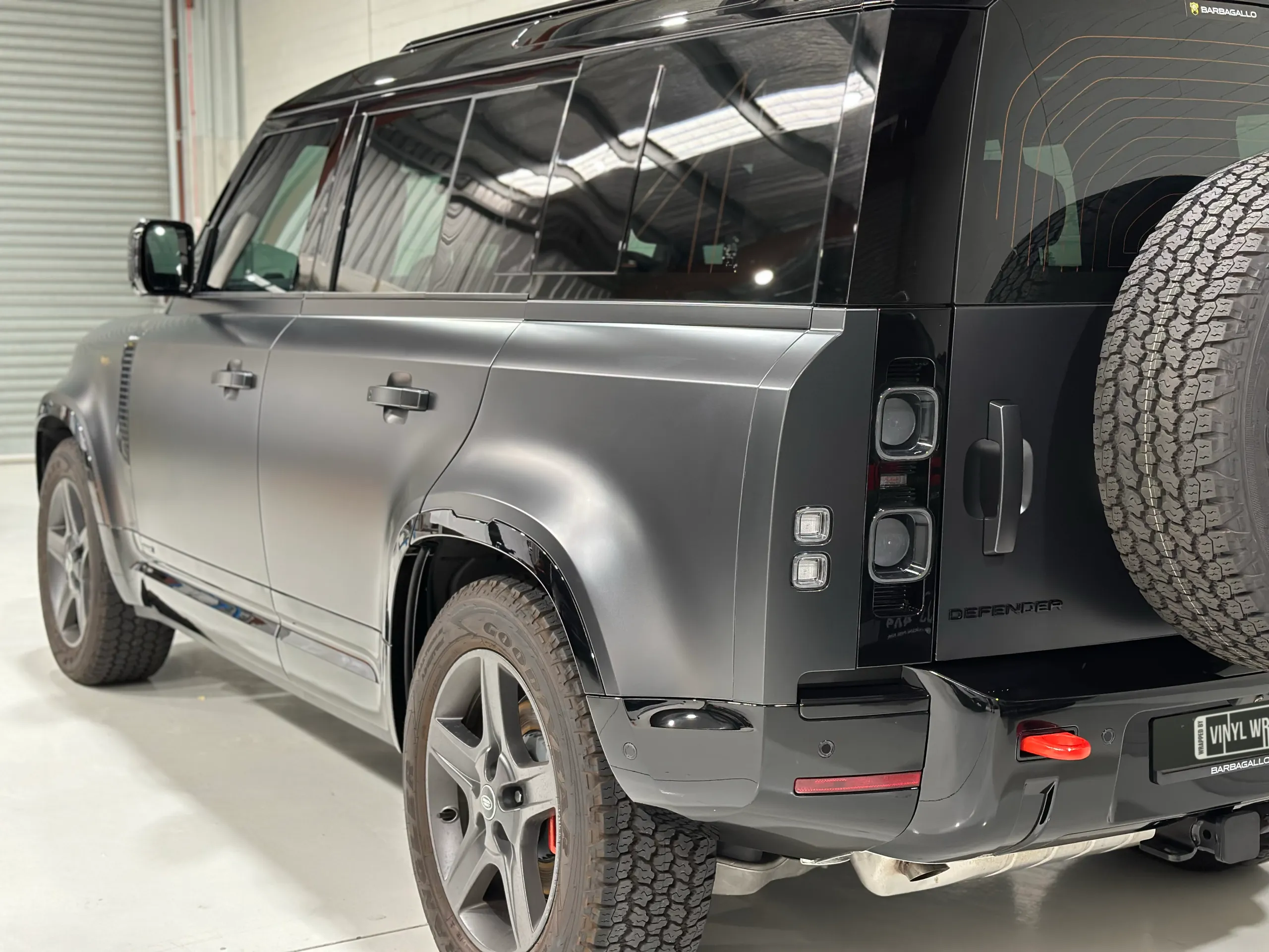 Land Rover Defender rear quarter showing matte grey doors, gloss black trim and its exposed spare tyre