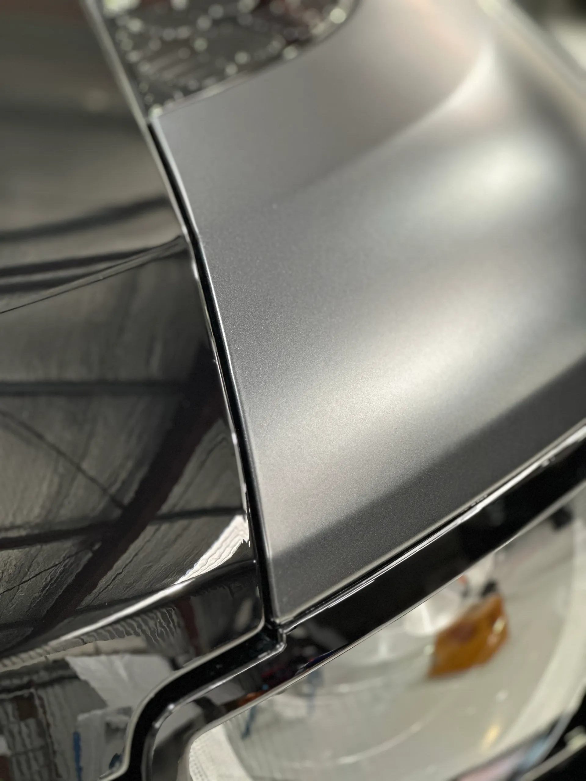 Close-up of the boundary between the glossy black bonnet and matte grey guard above a Defender headlight