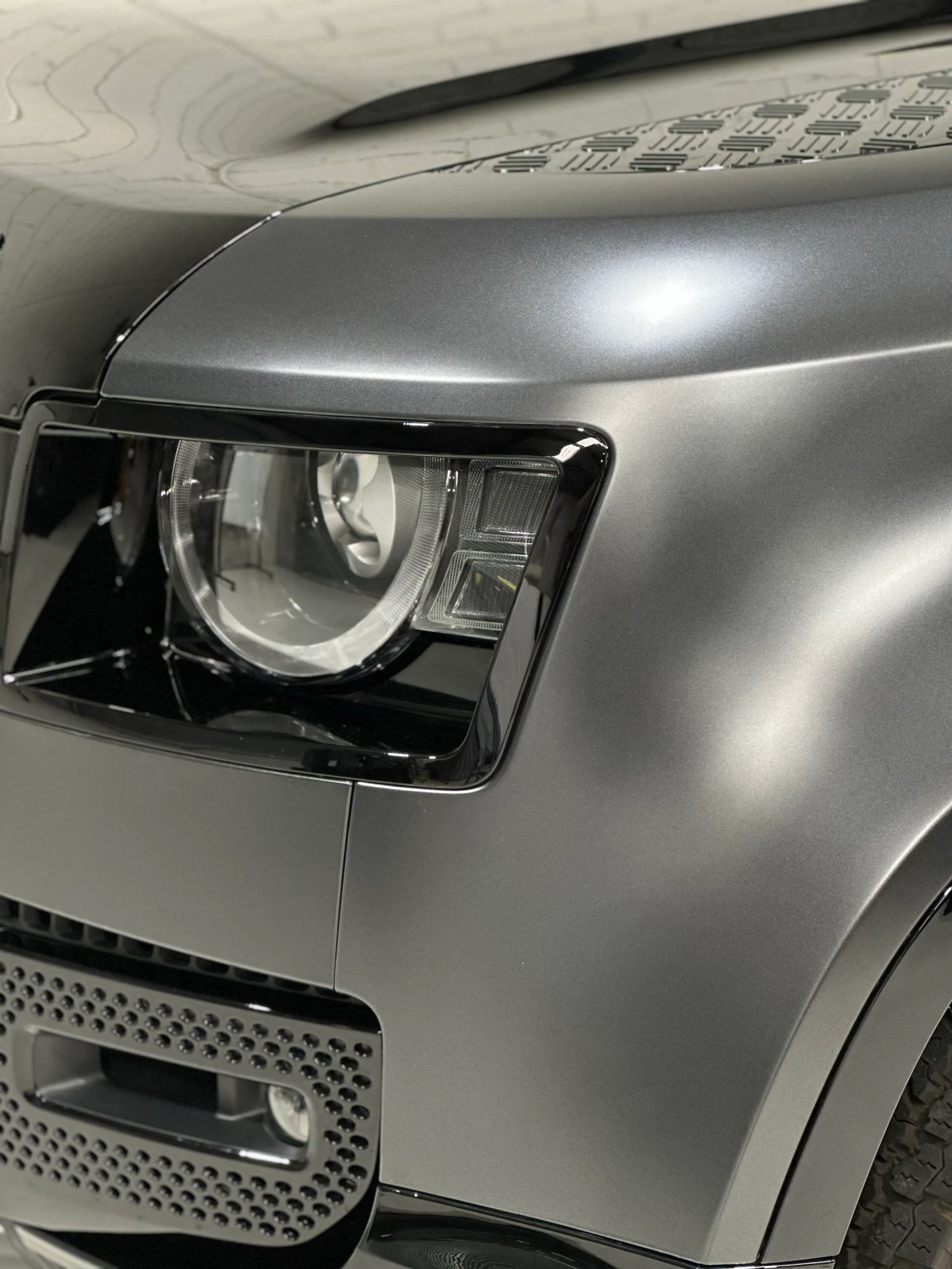 Detail of a Land Rover Defender headlight and matte grey guard with a textured panel above