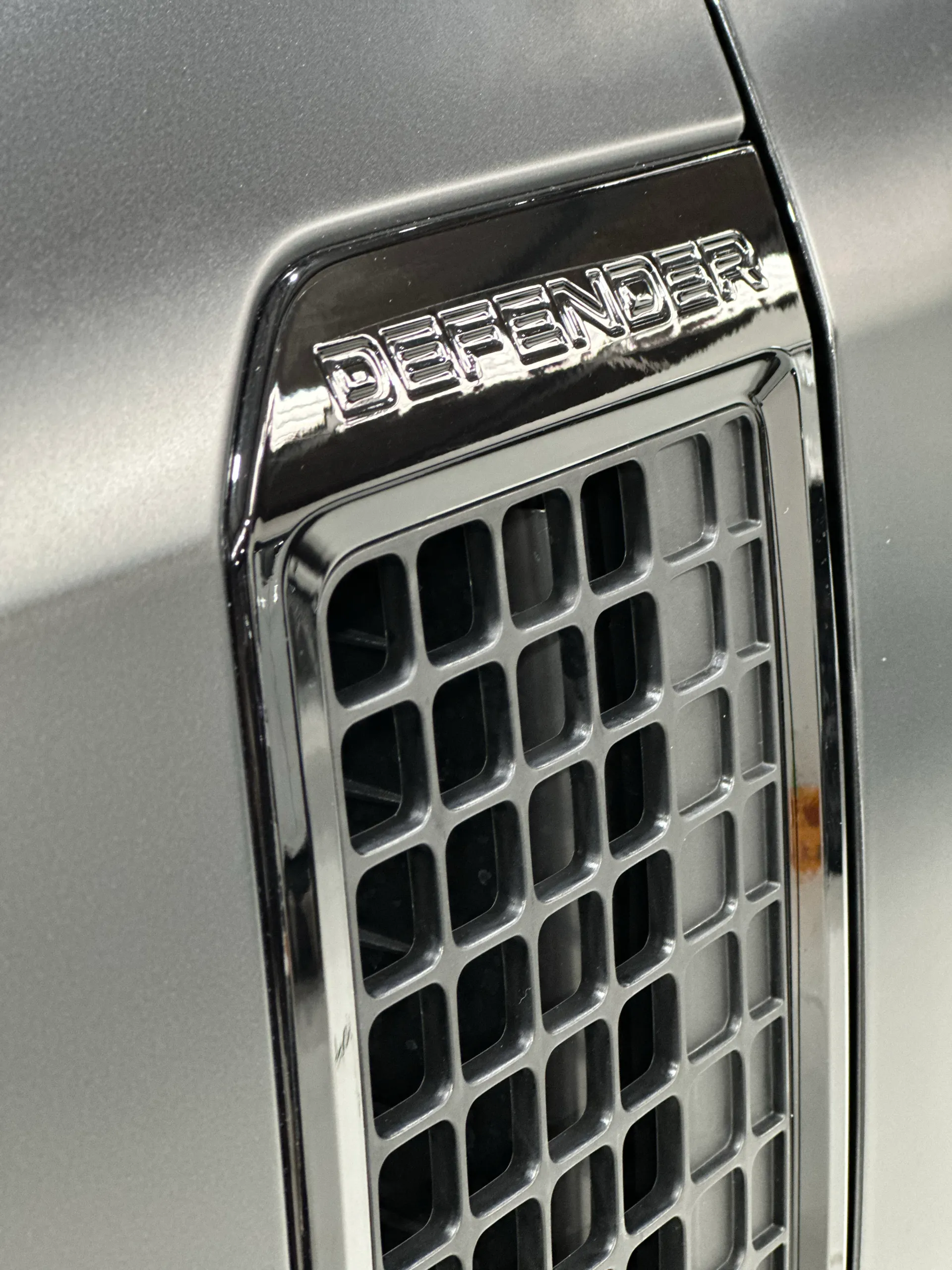 Defender lettering on the gloss black front-guard vent beside matte grey bodywork