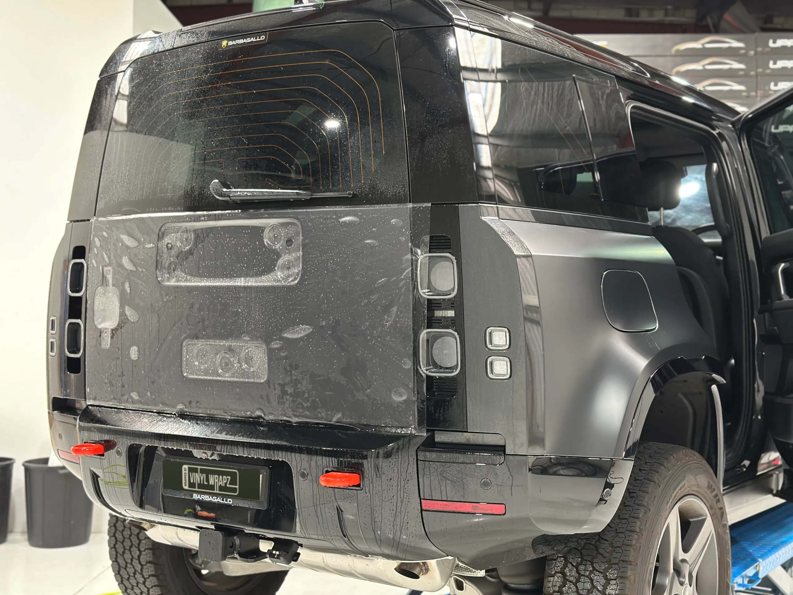 Land Rover Defender rear during film installation, with wet film across the tailgate and spare wheel removed