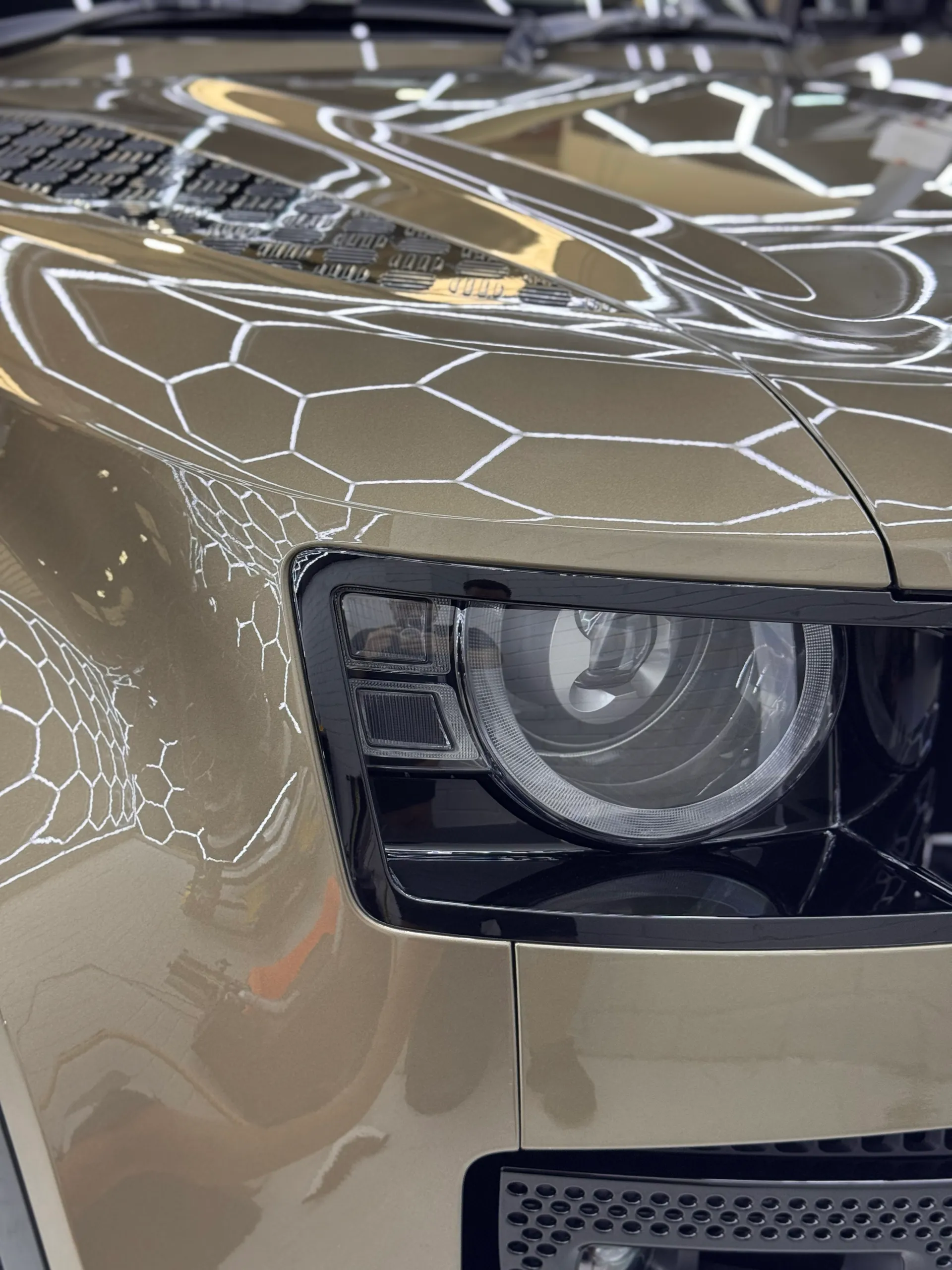 Gloss bronze Land Rover Defender headlight and bonnet reflecting hexagonal workshop lights