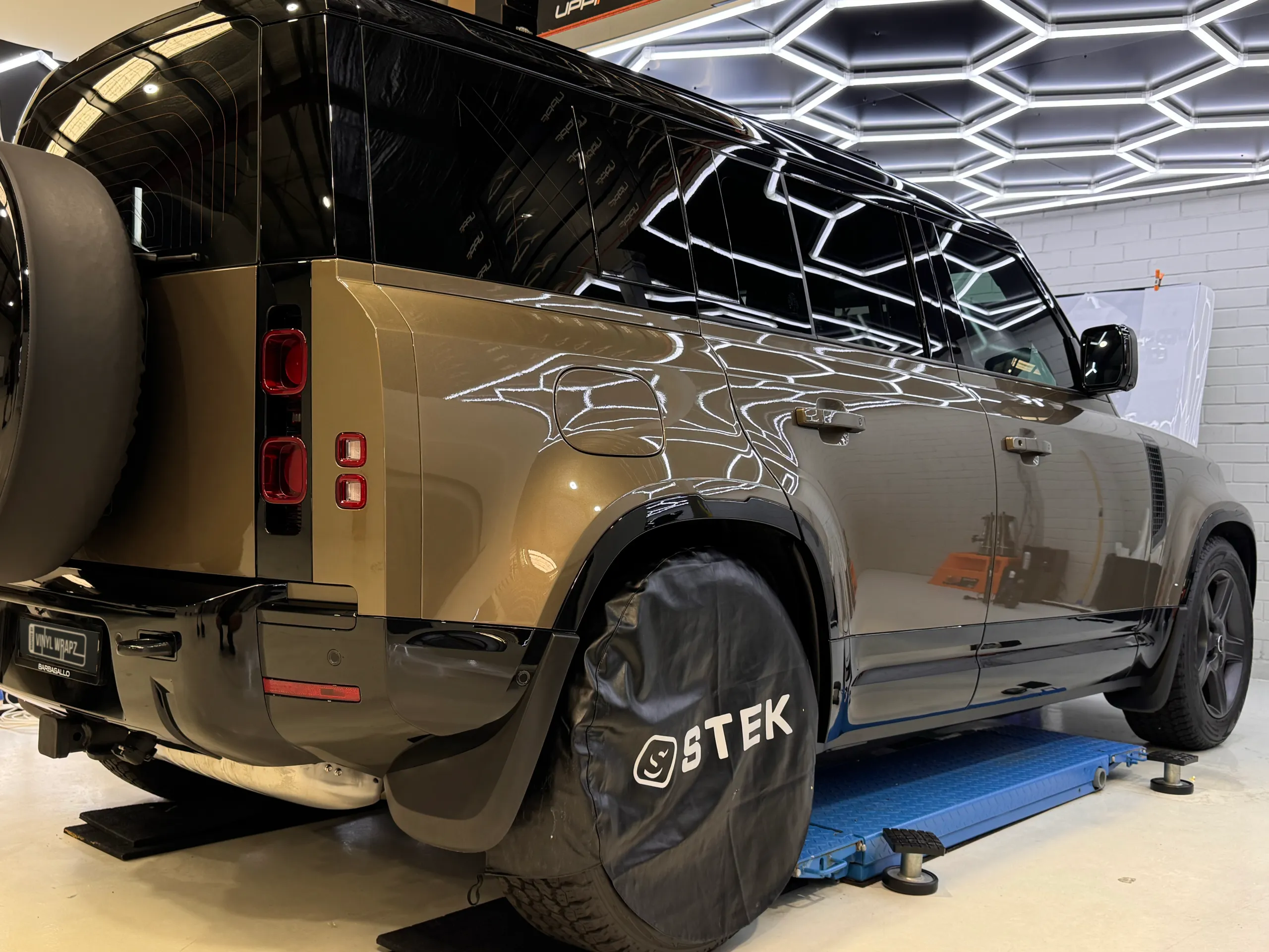 Bronze Land Rover Defender on a workshop lift with its rear wheel covered during preparation