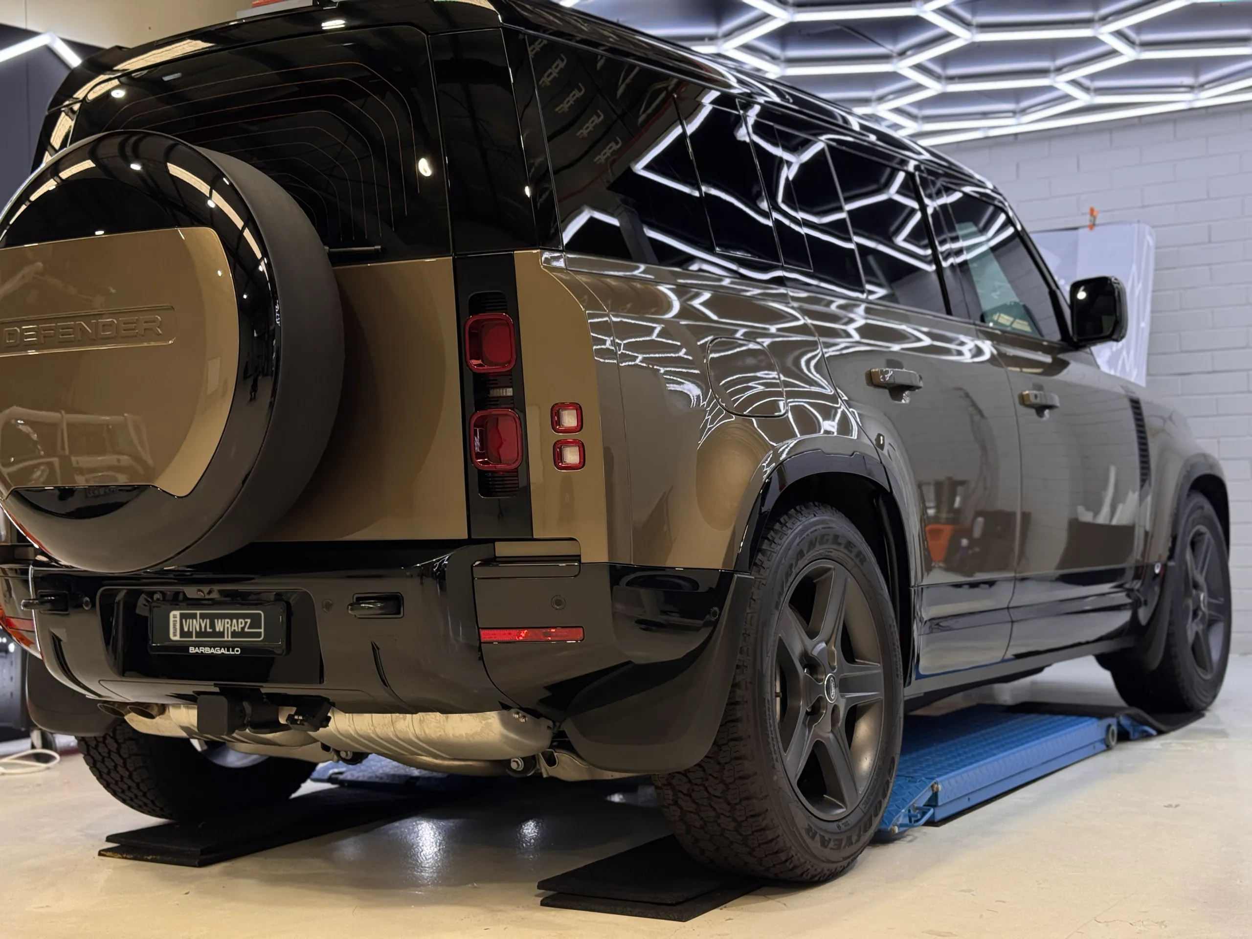 Gloss bronze Land Rover Defender with a black roof, viewed from the rear quarter in the workshop