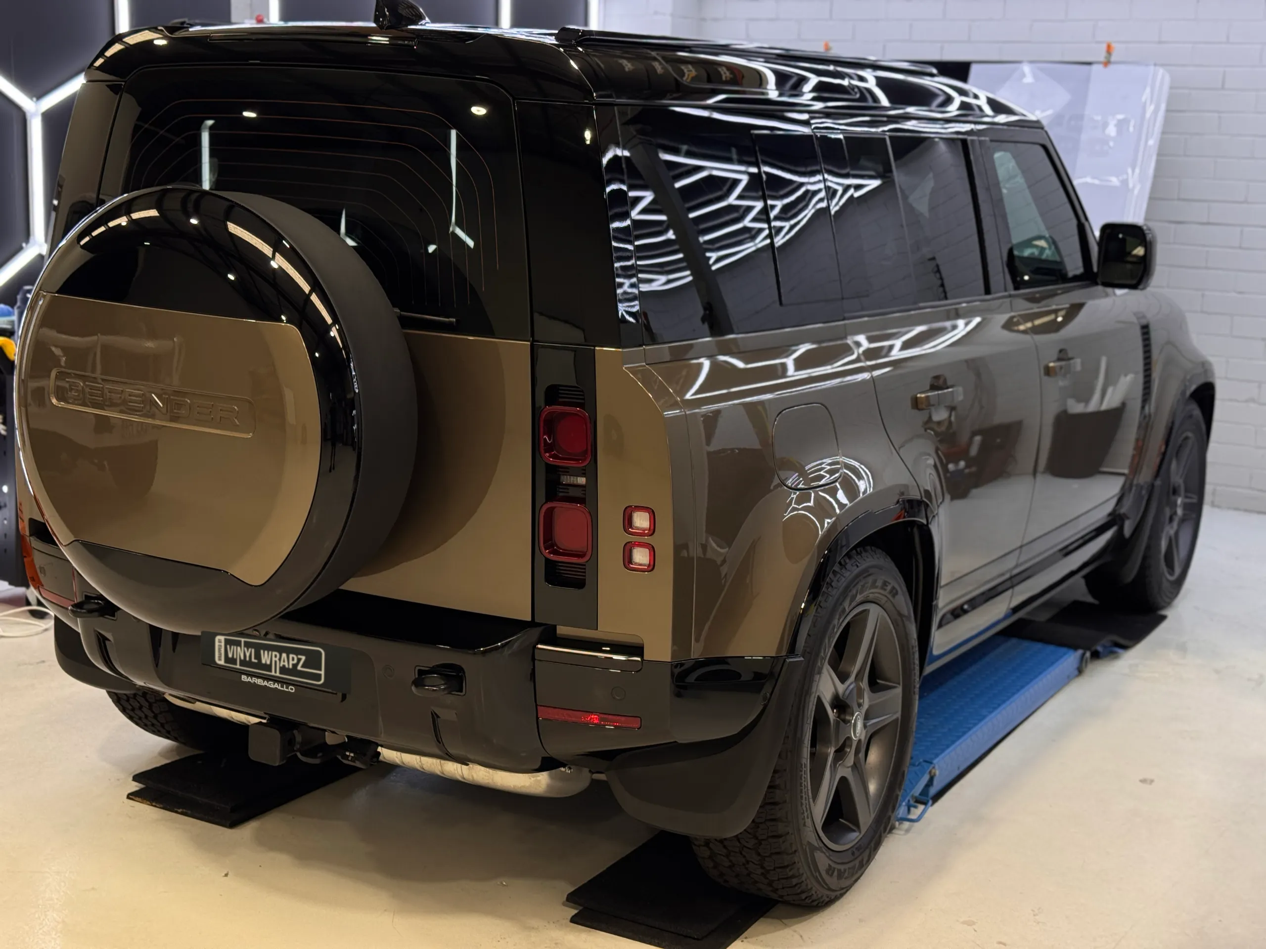 Rear-quarter view of the bronze Land Rover Defender spare-wheel cover and black upper body