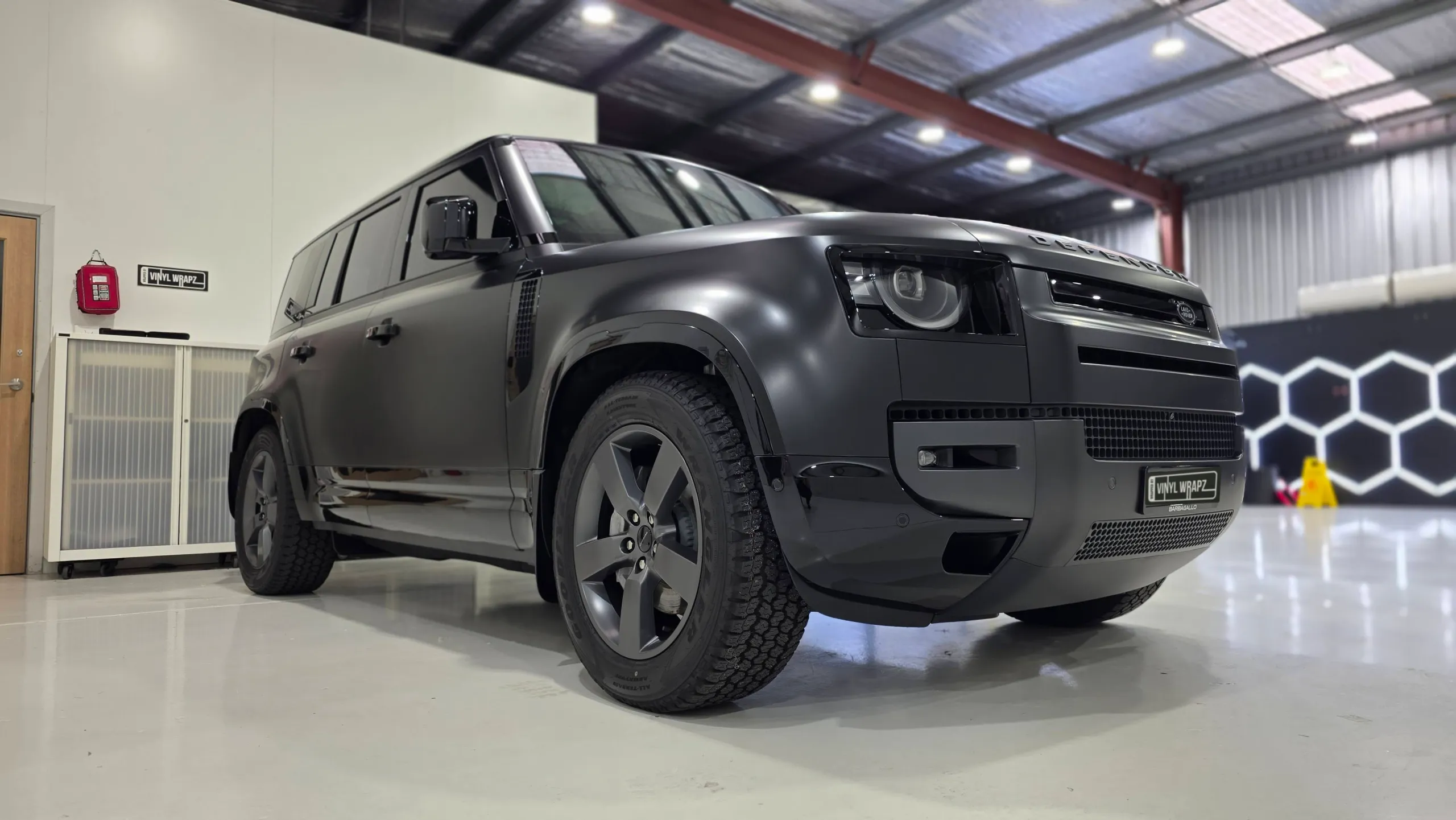 Matte dark grey Land Rover Defender viewed from a low front-quarter angle in the workshop