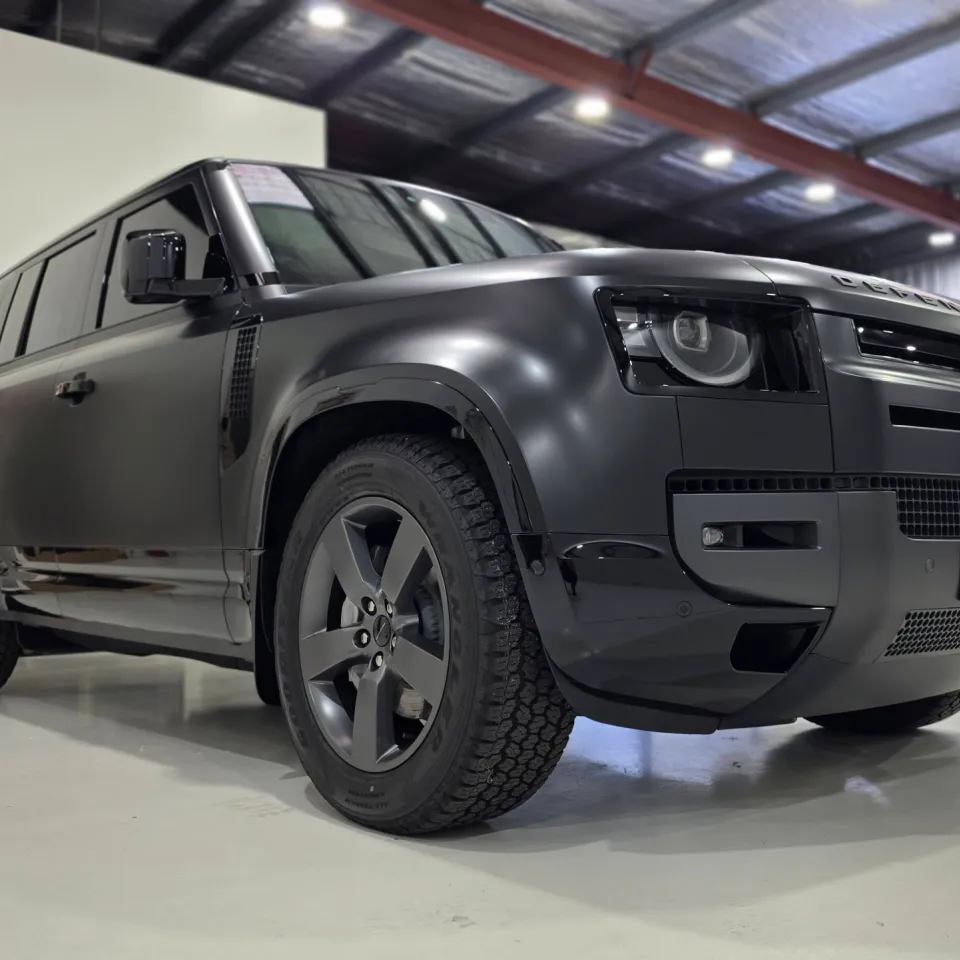 Matte dark grey Land Rover Defender viewed from a low front-quarter angle in the workshop