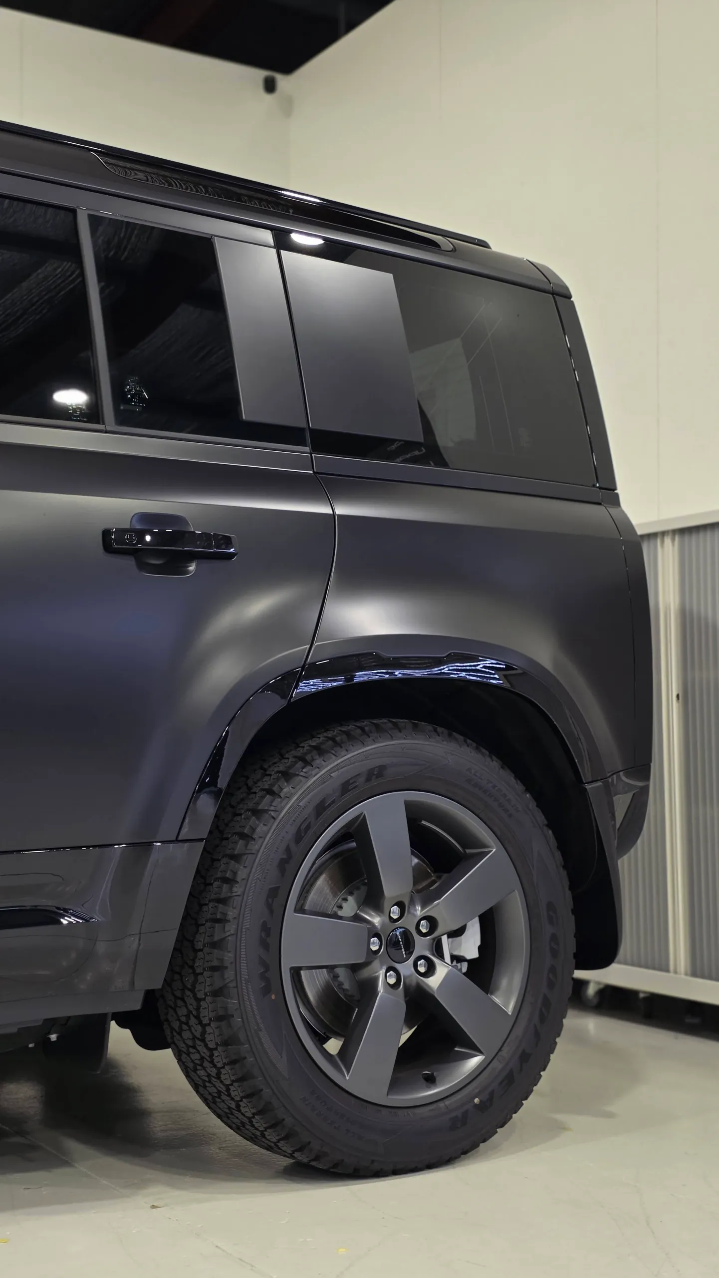 Land Rover Defender rear wheel and matte dark grey rear door beside gloss black trim
