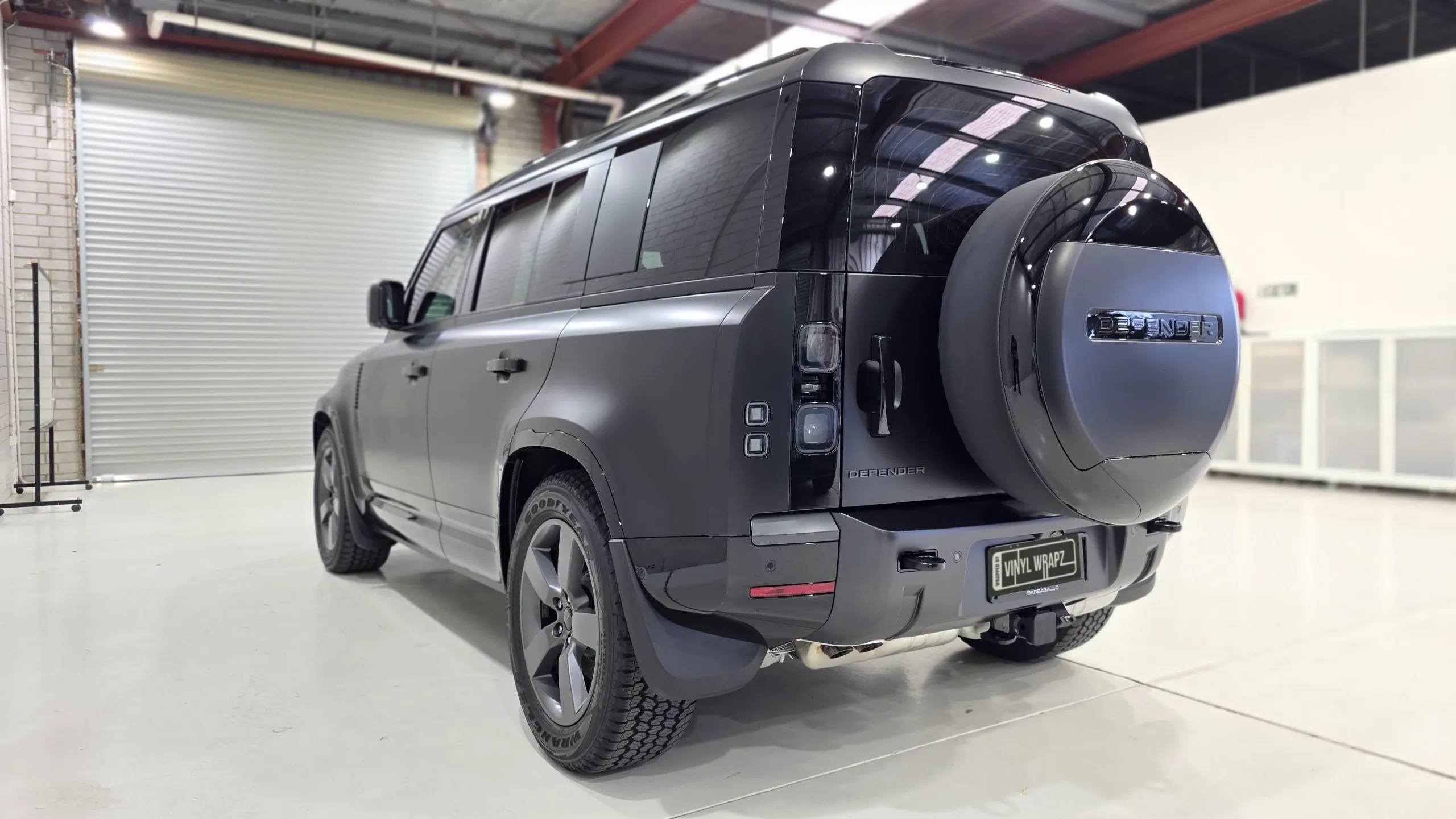 Matte dark grey Land Rover Defender viewed from the rear quarter in the workshop