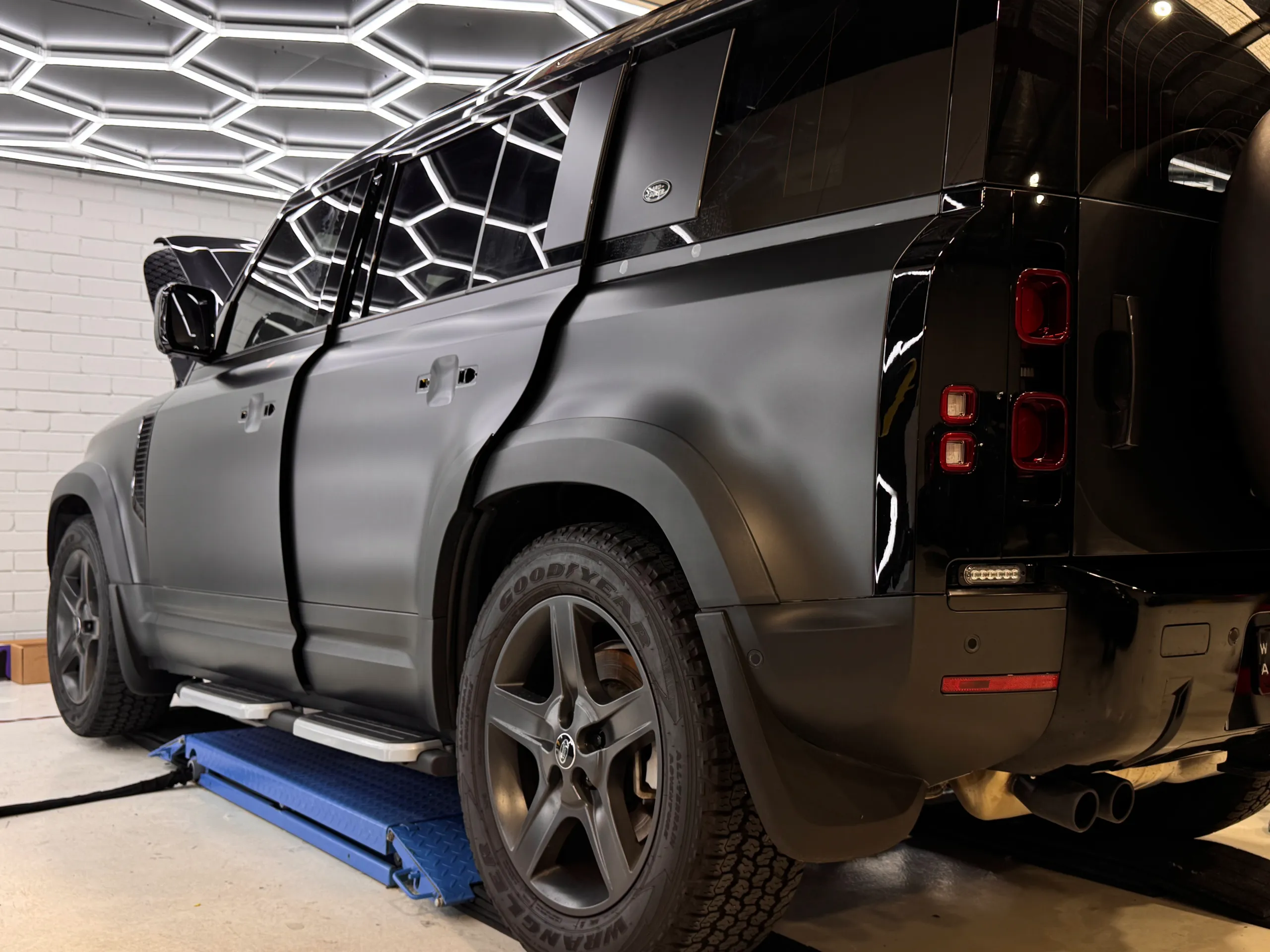 Land Rover Defender on a workshop lift during film work, with handles and rear trim removed