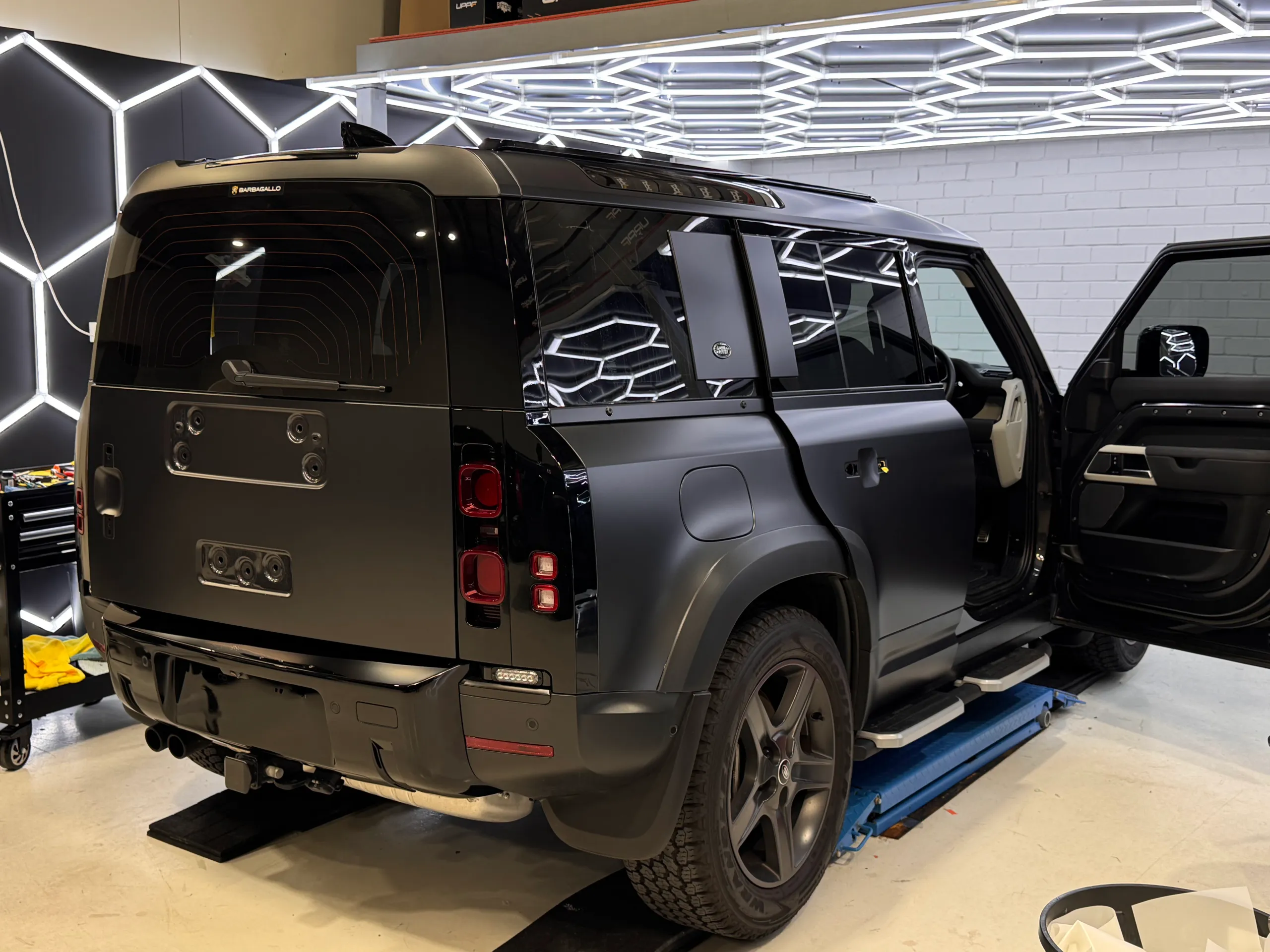 Land Rover Defender on a lift with its spare wheel and rear trim removed and front door open