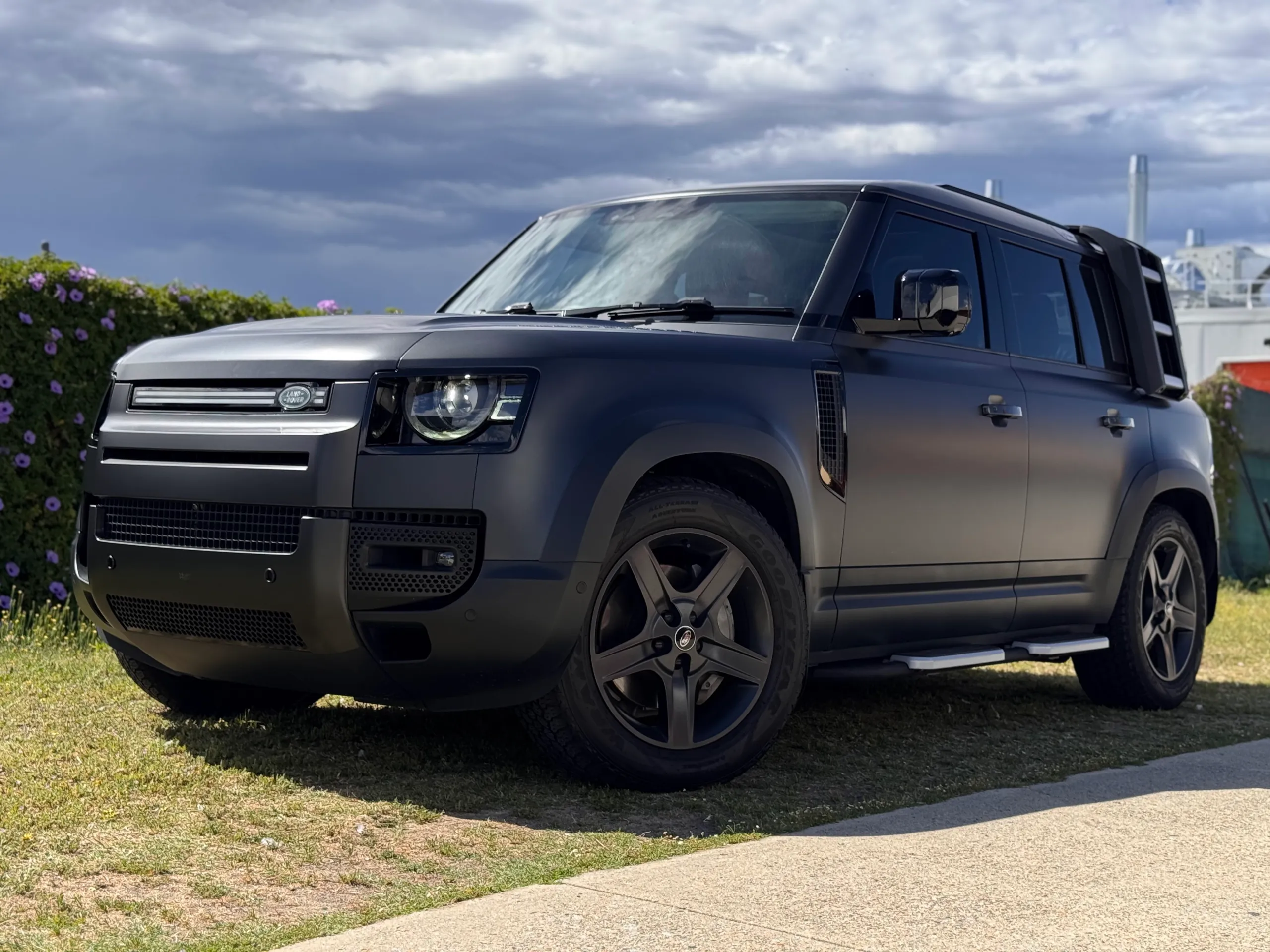 Matte dark grey Land Rover Defender in sunlight, with black wheels and side steps