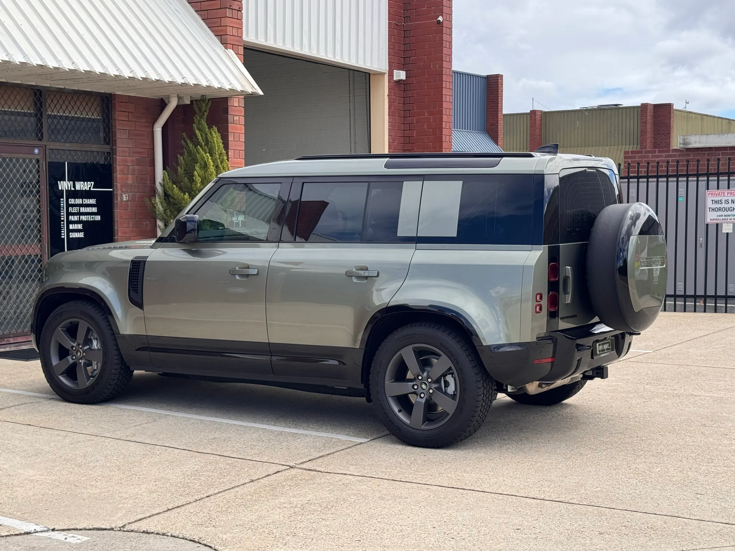 Pale green Land Rover Defender viewed from the side and rear outside the workshop