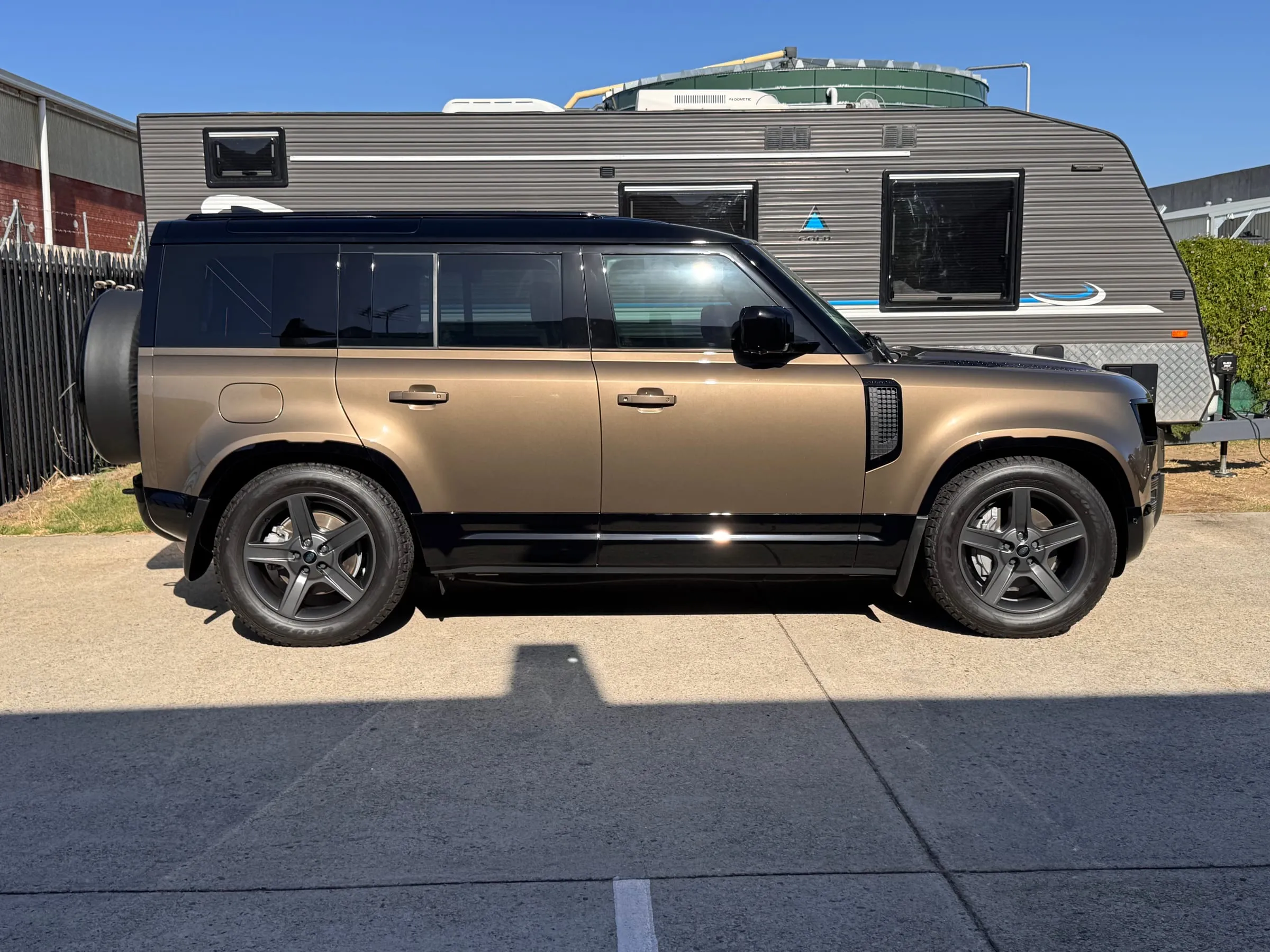 Bronze Land Rover Defender 110 with clear paint protection film, parked in front of a caravan outside the Vinyl Wrapz workshop