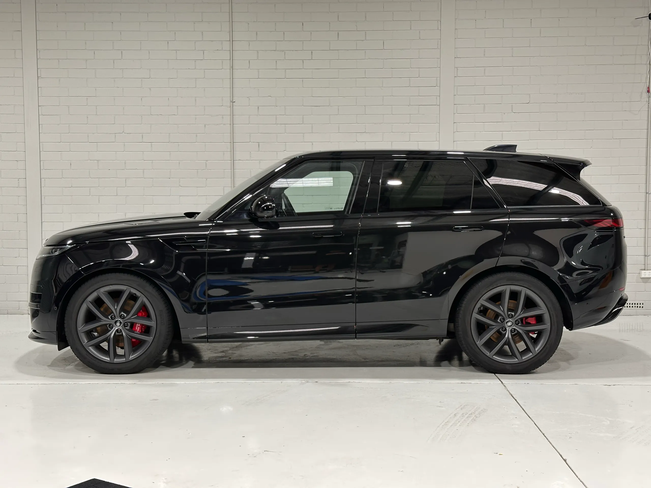 Side profile of the gloss black Range Rover Sport against a white workshop wall