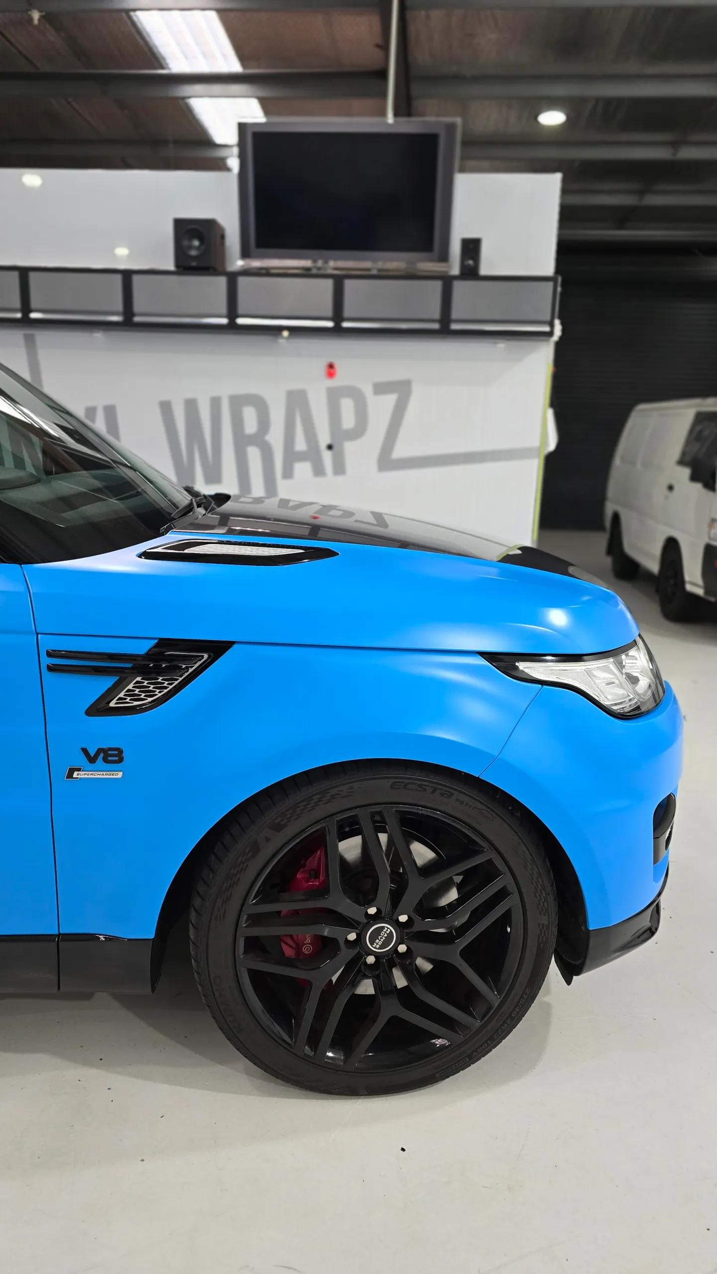Black front wheel and side vent against the satin blue Range Rover Sport guard
