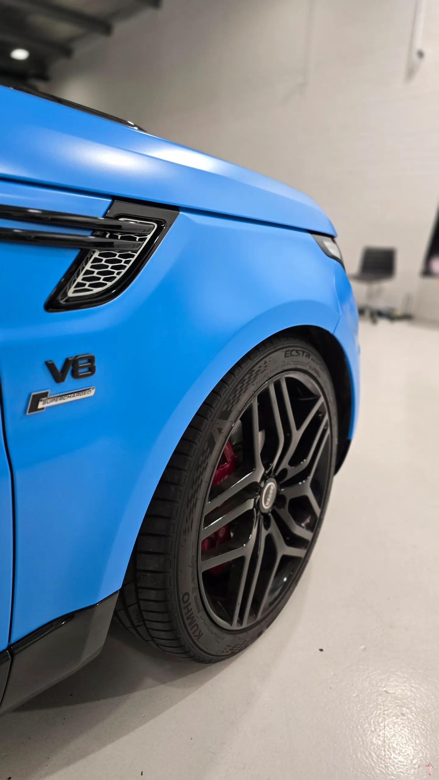 Range Rover Sport V8 badge, black side vent and wheel against satin blue bodywork