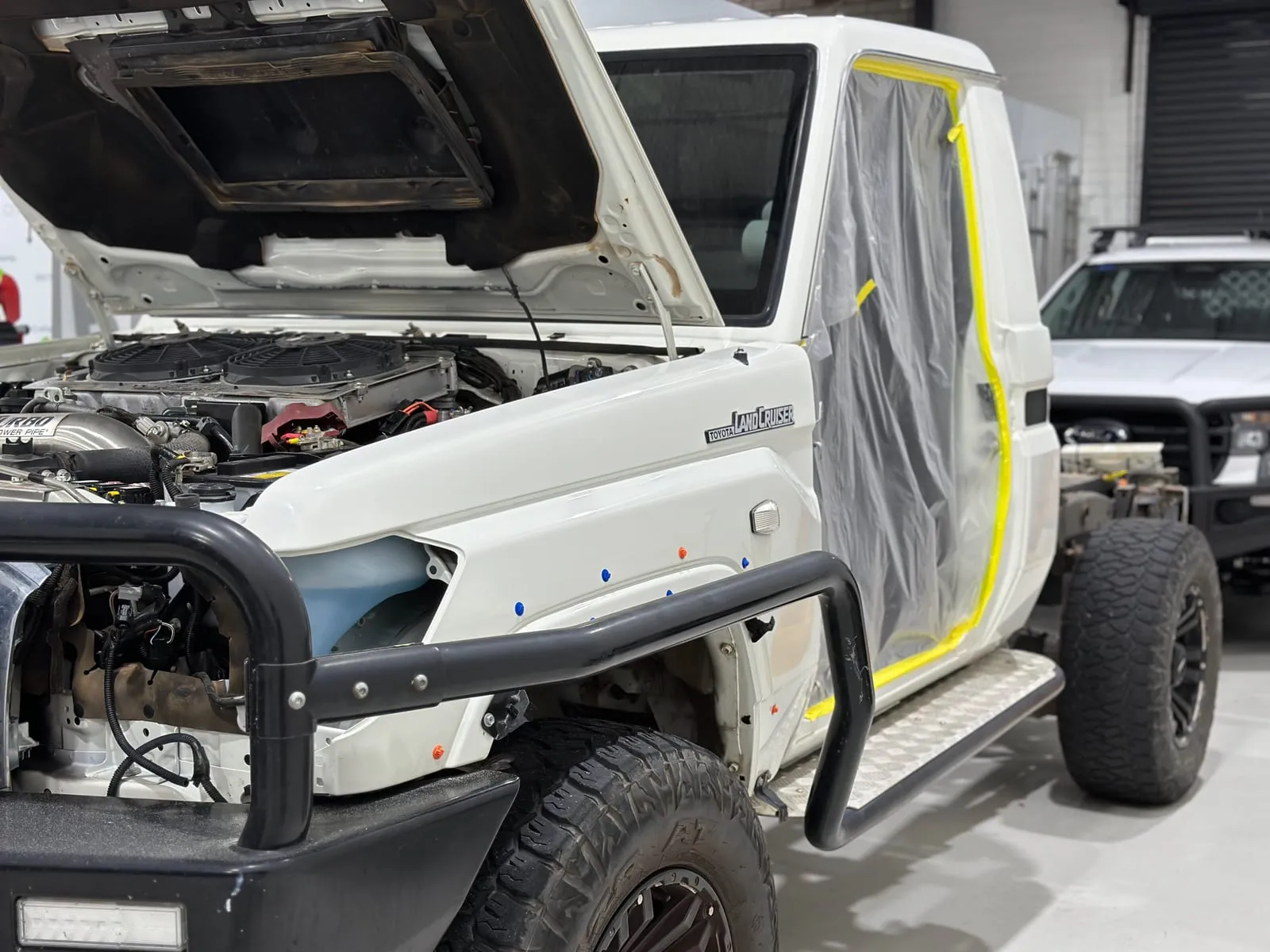 White Land Cruiser tray ute with the bonnet open, masked and prepped for a wrap in the workshop