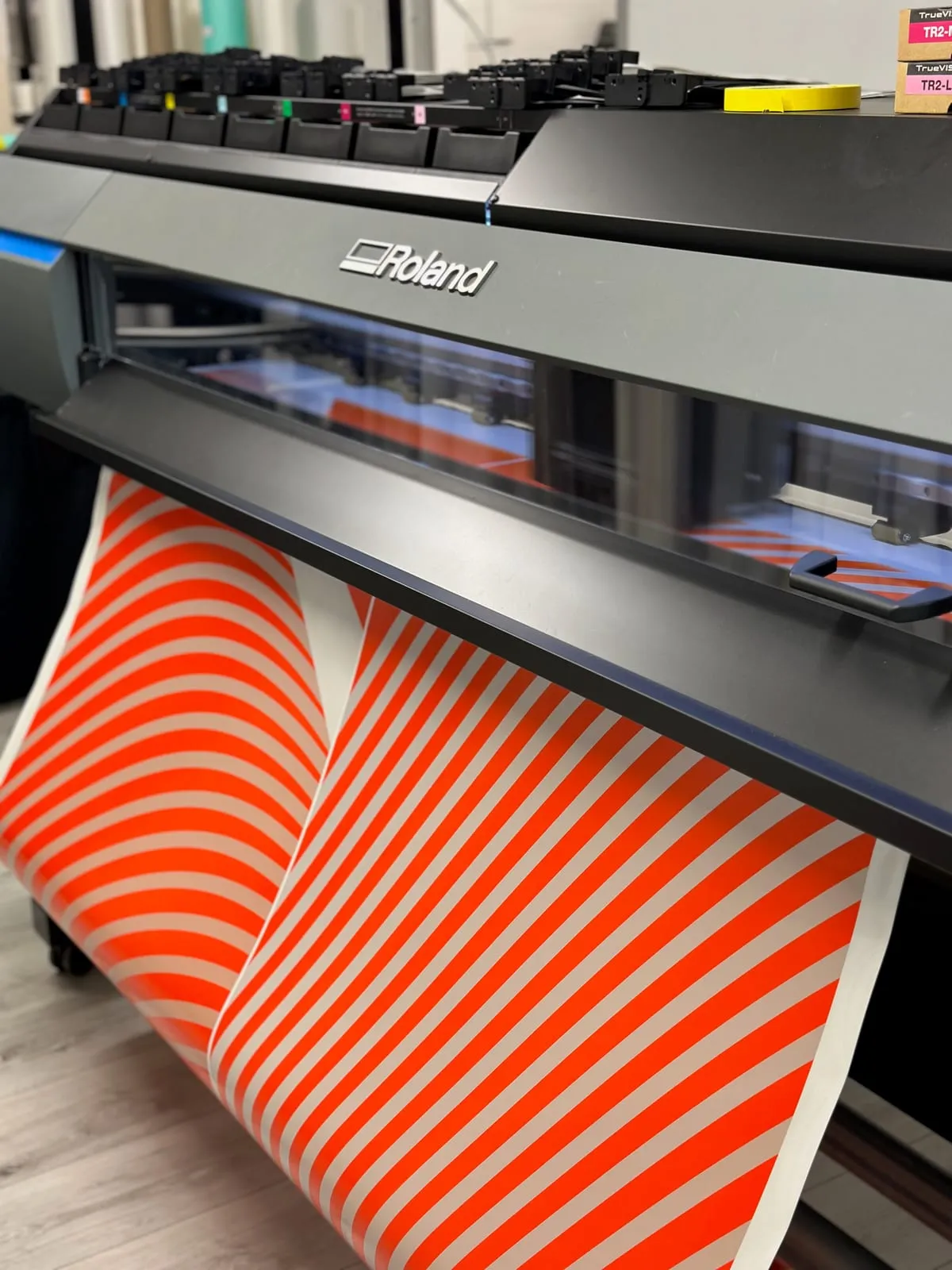 Large-format printer feeding out freshly printed orange and white striped vinyl film
