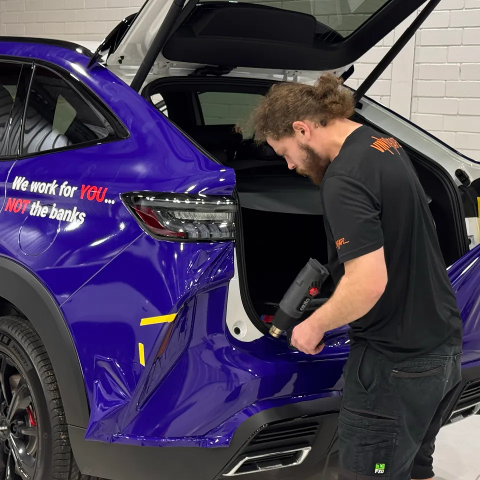 Installer heating purple film around the rear bumper of a Lenda Finance SUV with the tailgate open