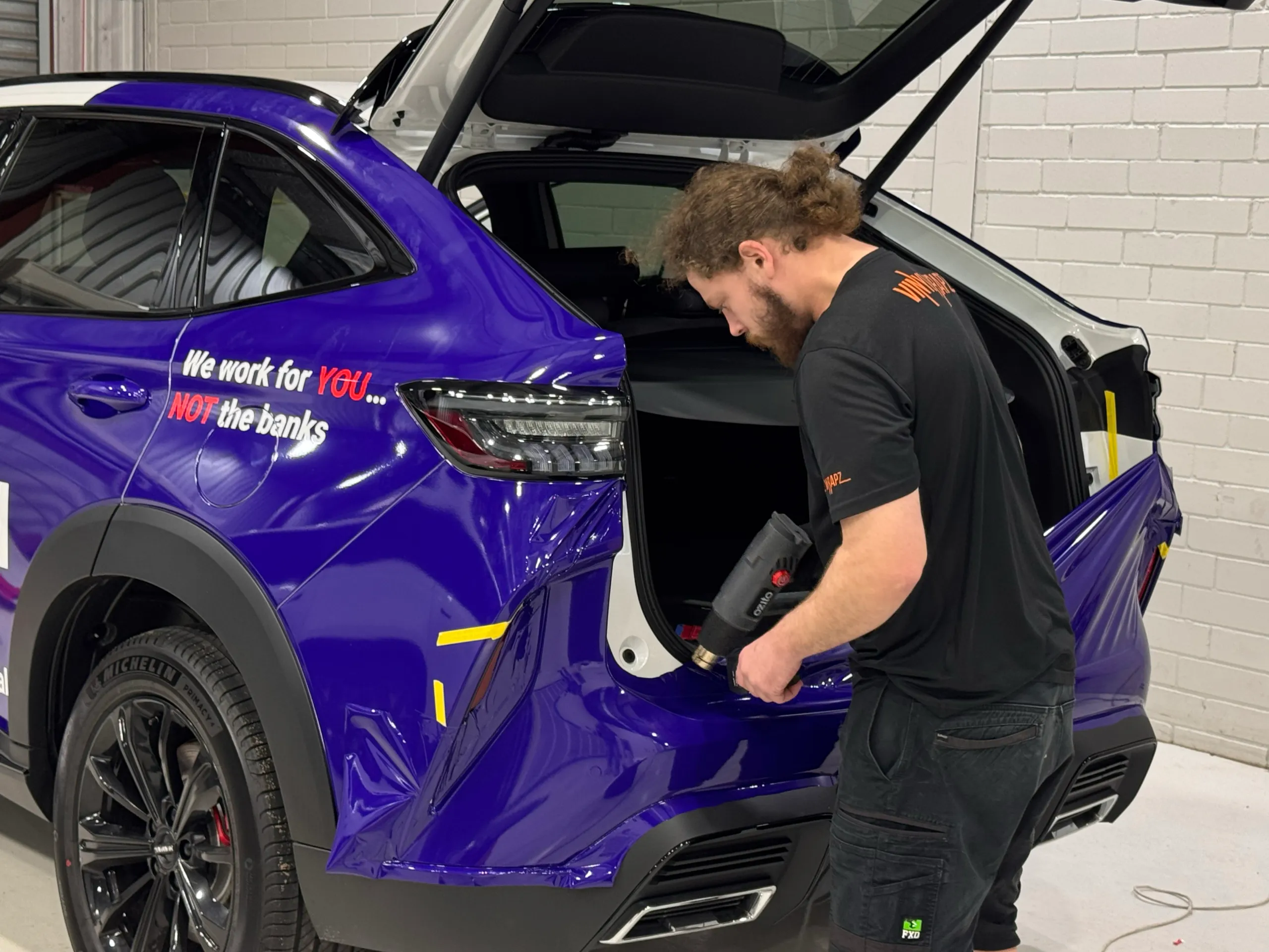 Installer heating purple film around the rear bumper of a Lenda Finance SUV with the tailgate open