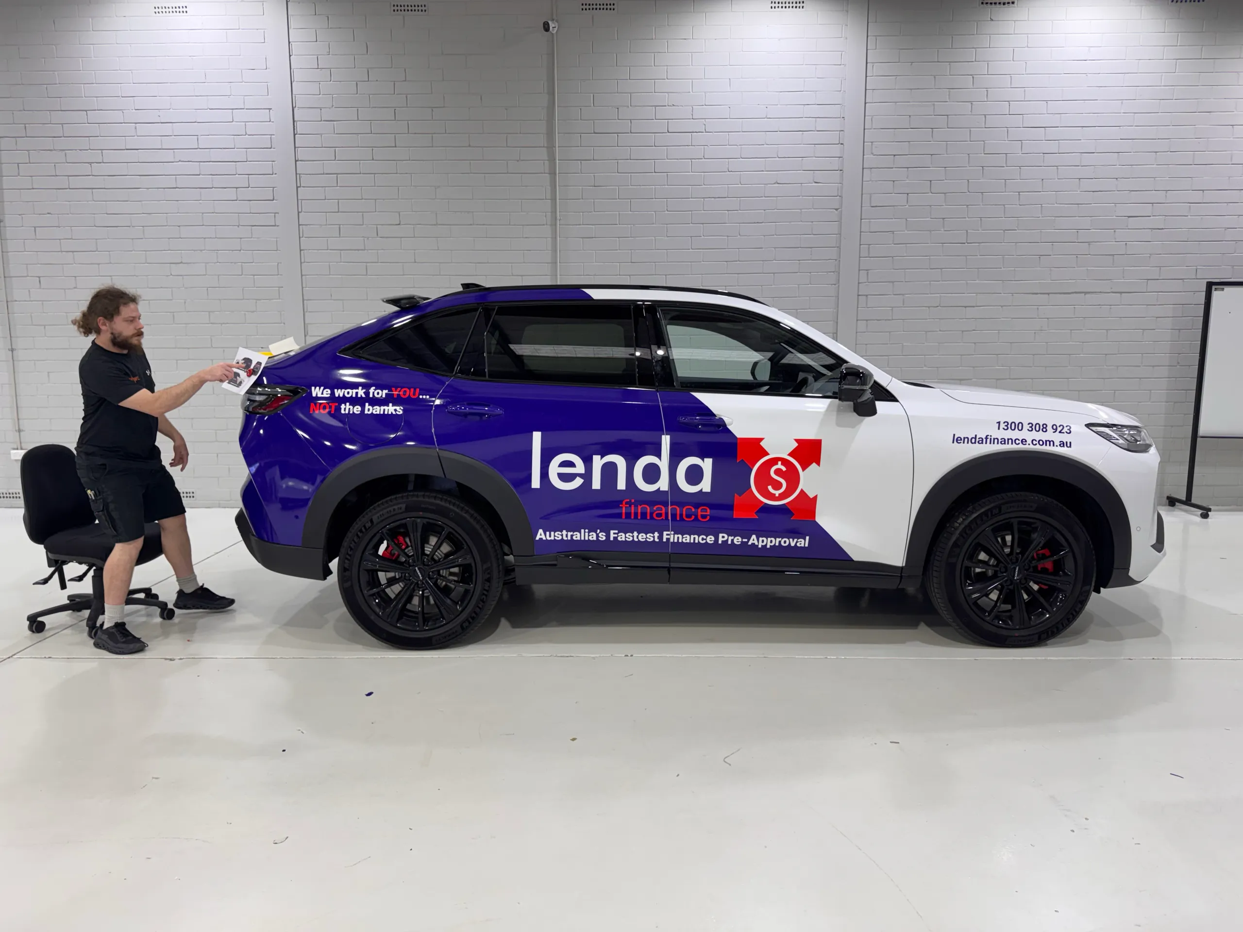 Installer working beside a purple and white Lenda Finance SUV in the workshop