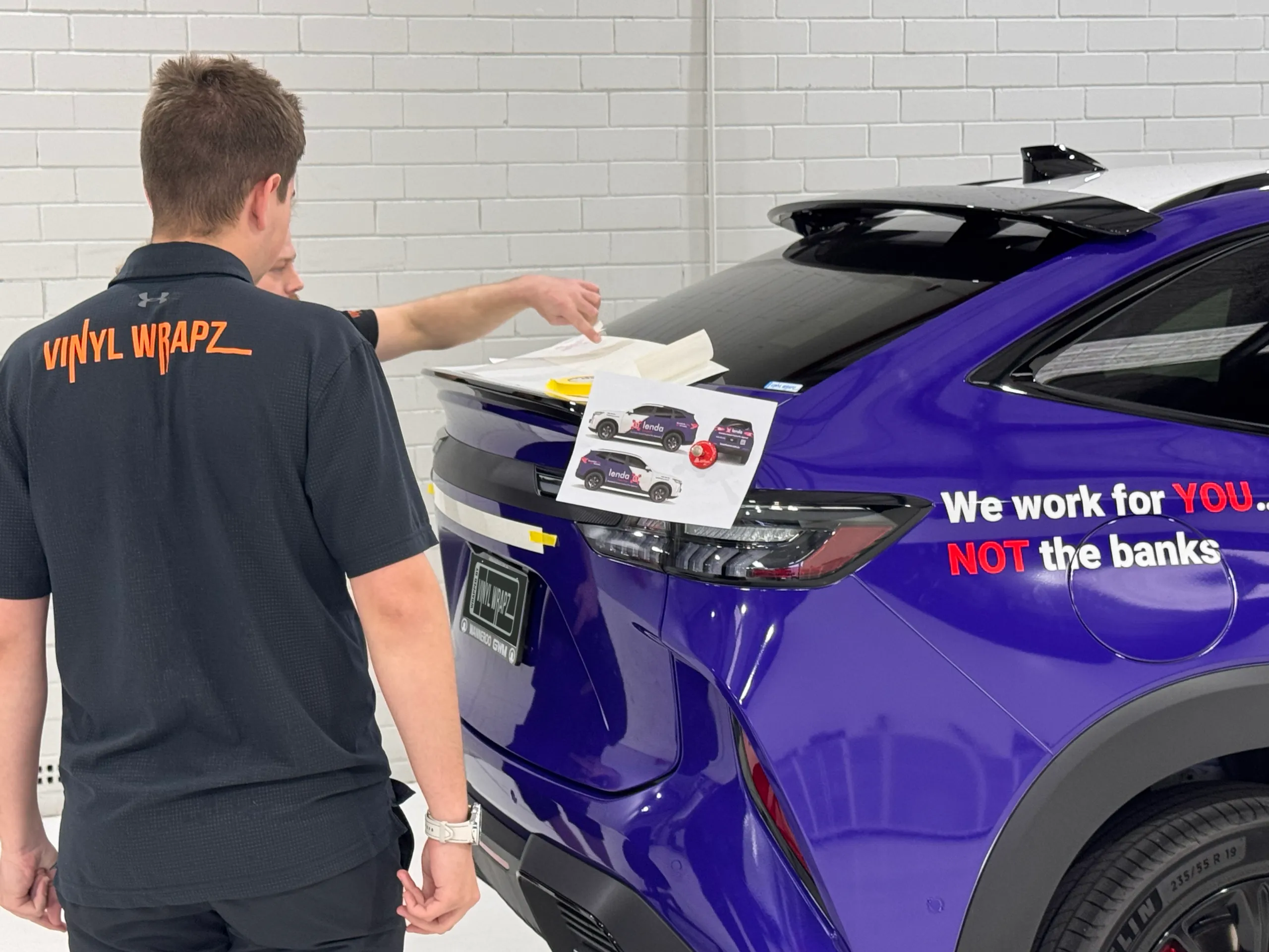 Installers checking Lenda Finance graphics beside the SUV rear quarter and tailgate