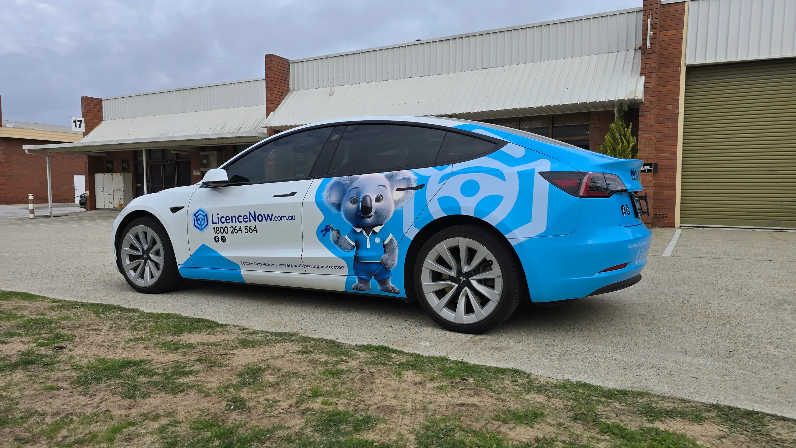 Blue and white LicenceNow Tesla Model 3 partial wrap, viewed from the rear quarter outdoors