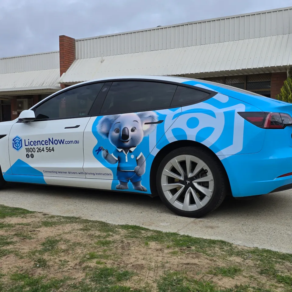 Blue and white LicenceNow Tesla Model 3 partial wrap, viewed from the rear quarter outdoors