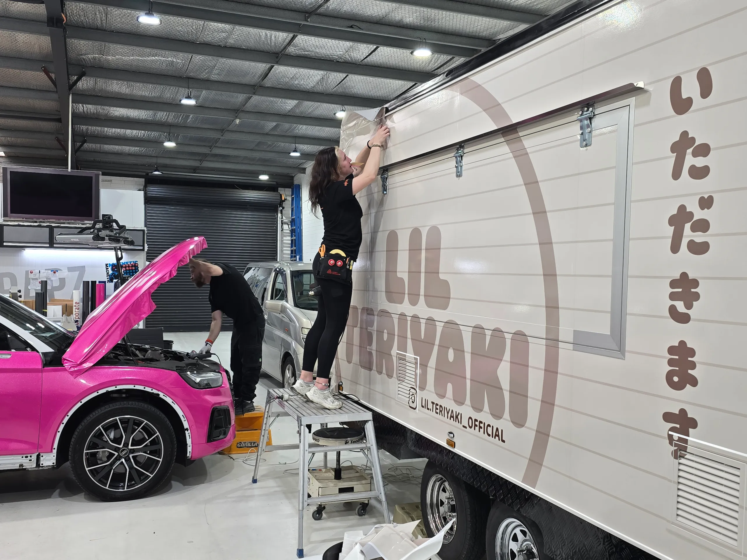 Installer fitting cream and brown Lil Teriyaki graphics along the top of a food trailer