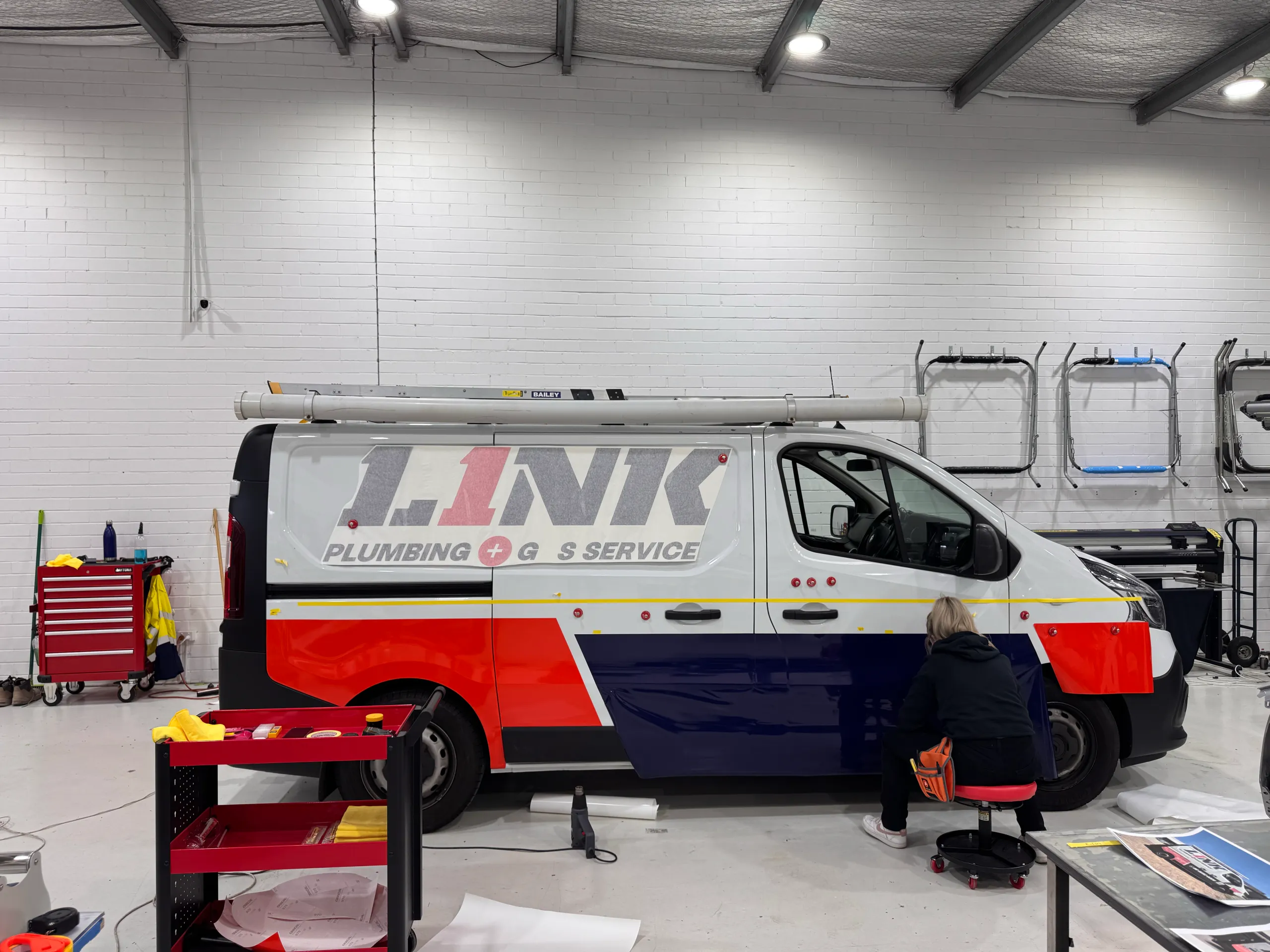 Installer facing away while fitting navy and orange-red Link Plumbing graphics to a white van