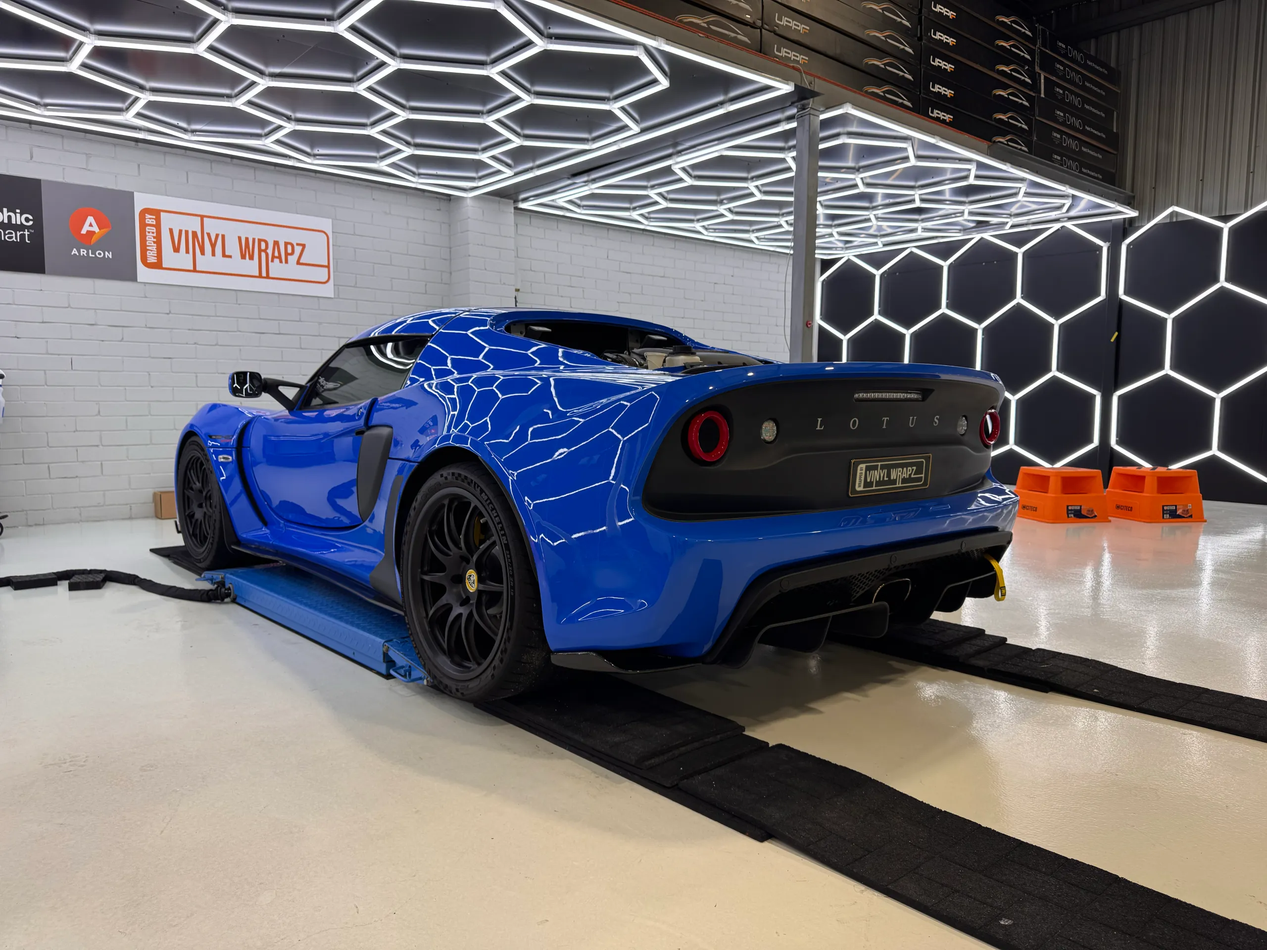Blue Lotus Exige on a workshop lift with its rear wing removed during preparation